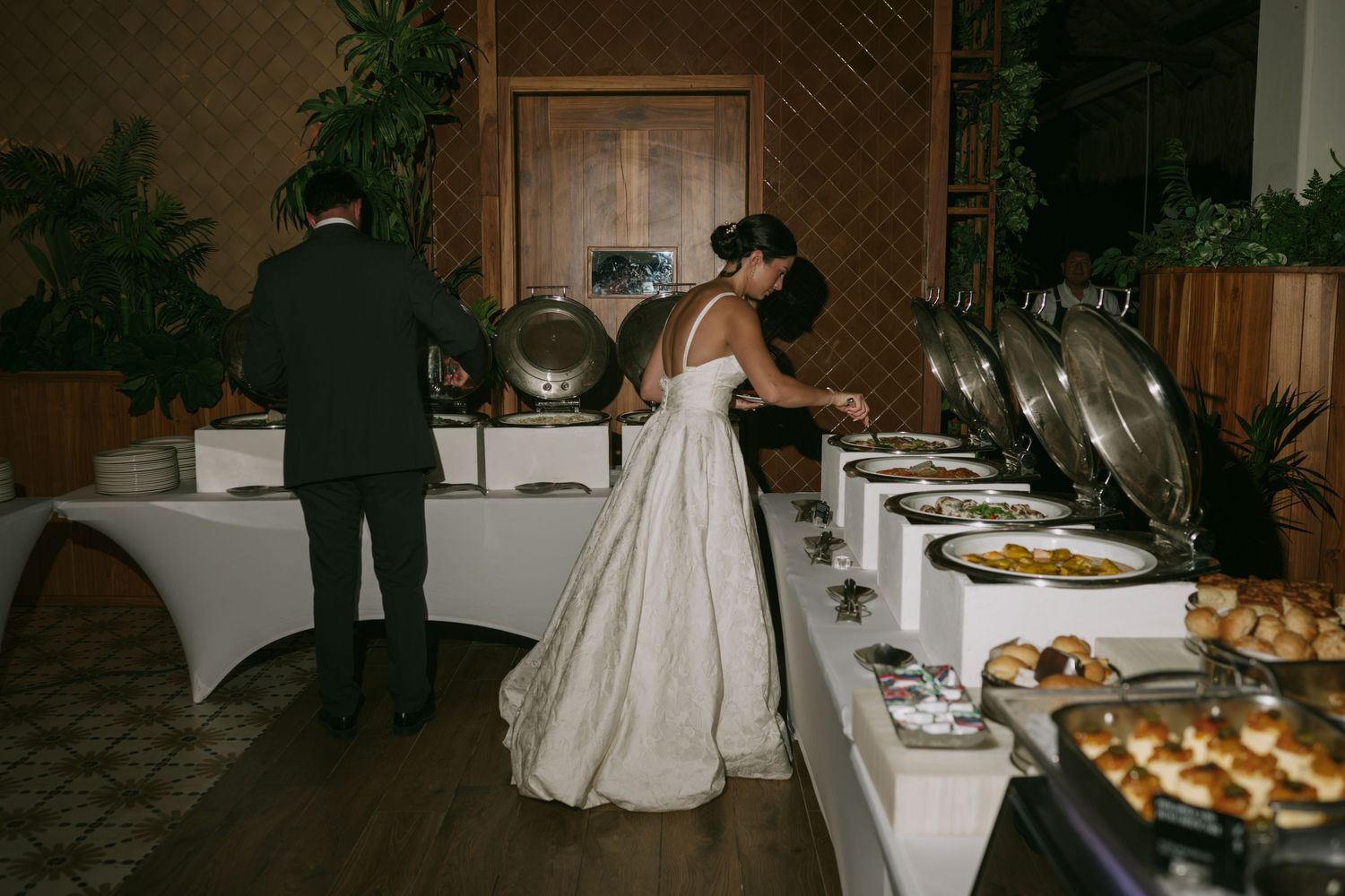 A wedding reception dessert table features an elegant display of pastries and treats arranged on white tablecloths.