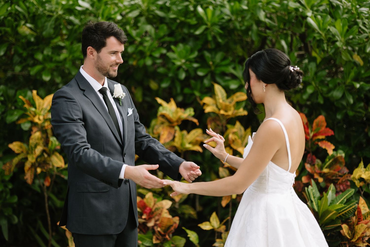 Bride and groom share a joyful first look moment in a lush garden setting with vibrant foliage.