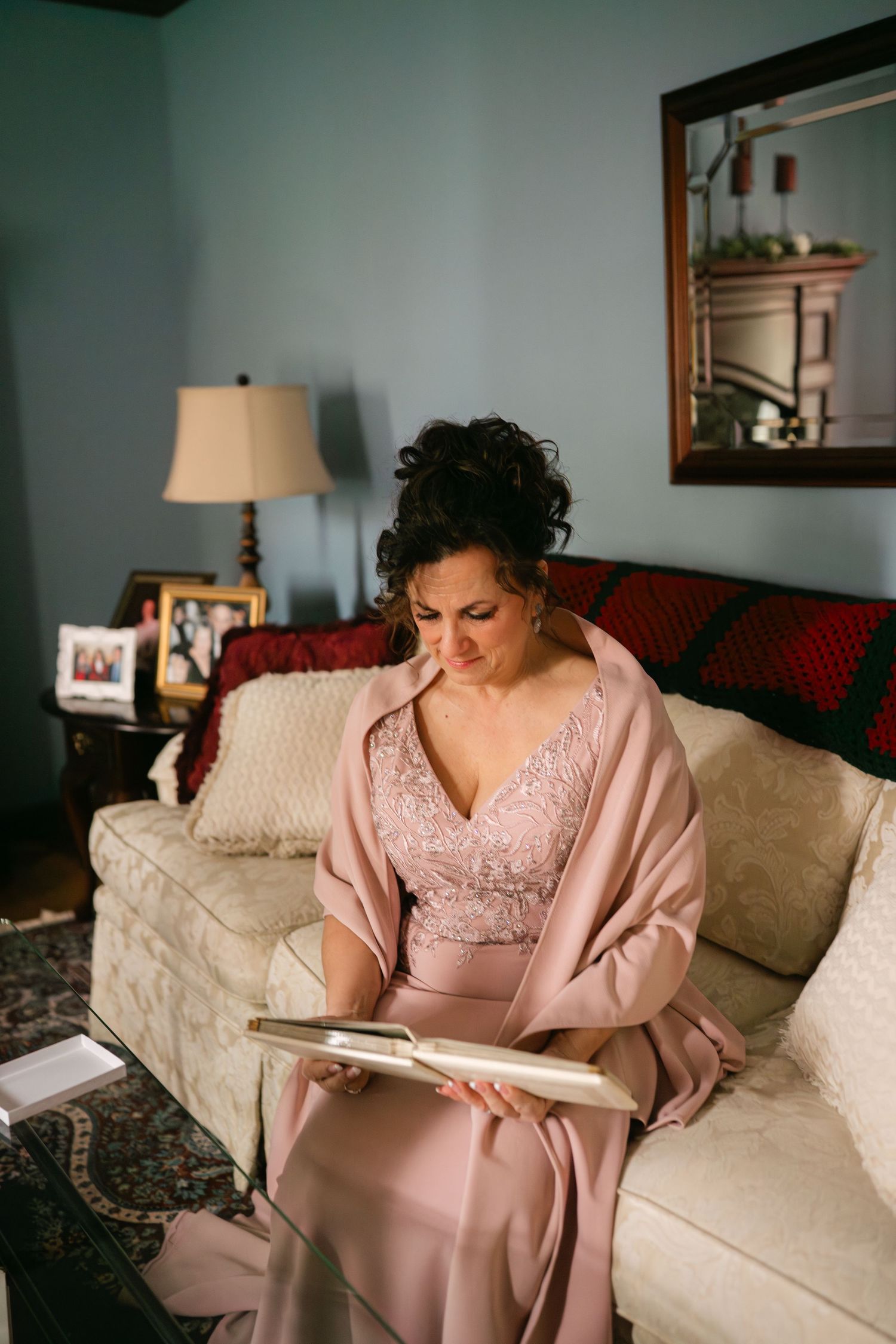 A person in a pink satin robe and lace nightgown relaxes on a beige couch while reading.