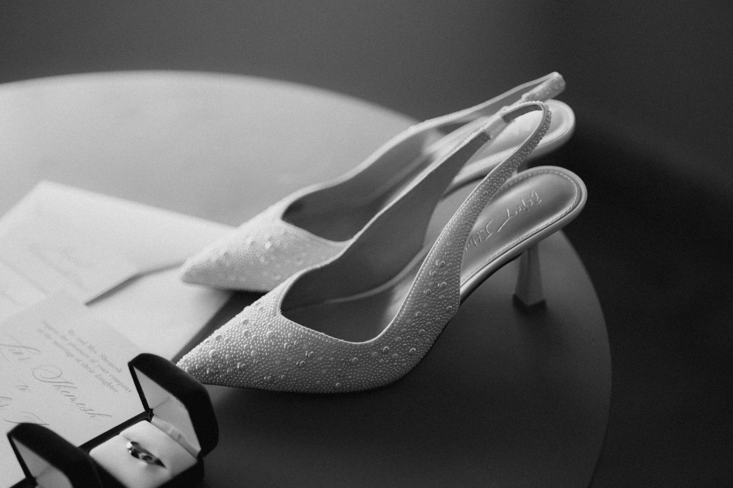 Black and white close-up detail of elegant bridal shoes with delicate embellishments.