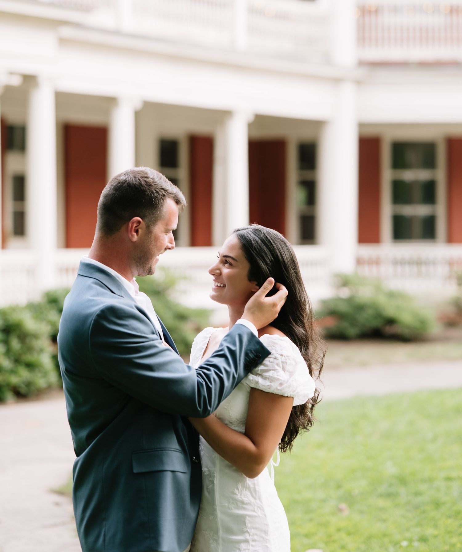 Romantic couple sharing a tender moment on a grassy lawn in front of a historic building.