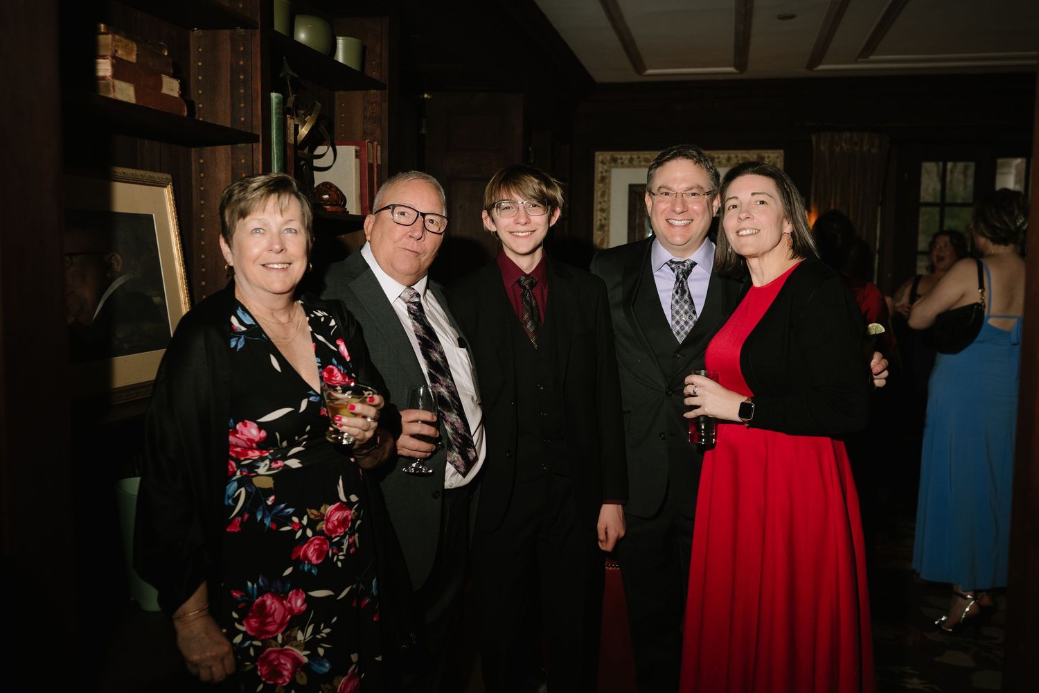 Group of five adults posing together at a formal event, smiling, dressed in elegant attire including a red dress.