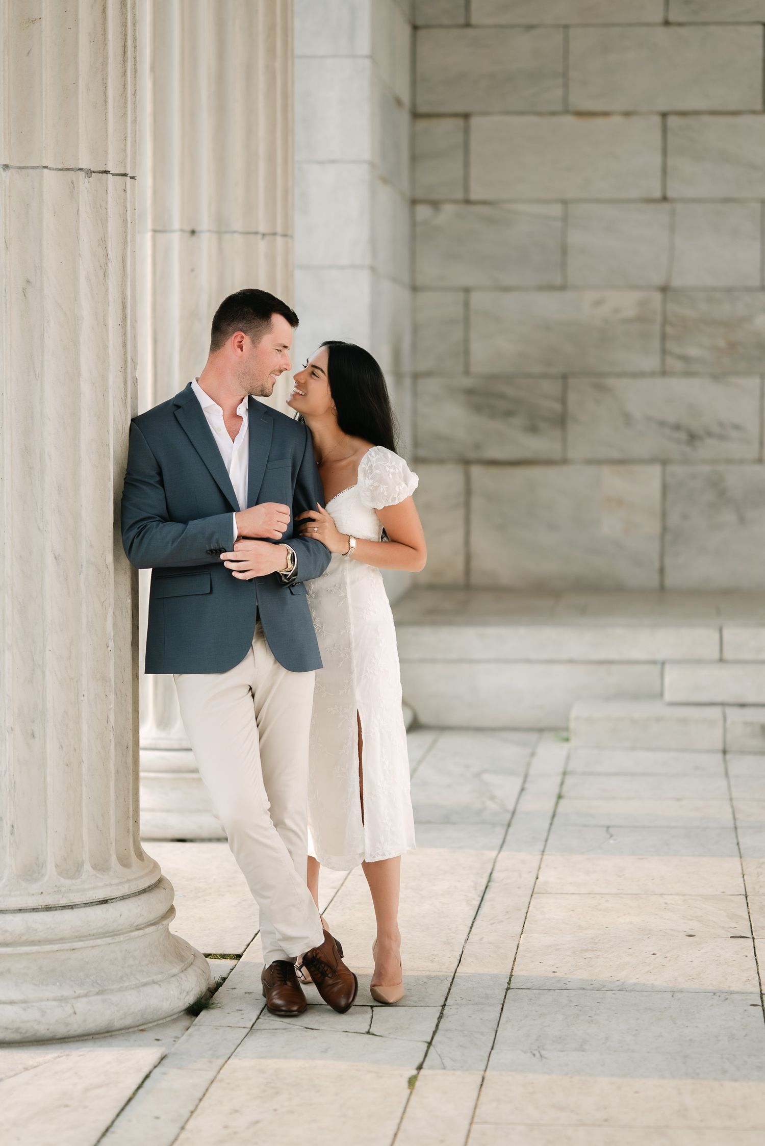 Playful engagement photos captured between elegant white pillars in natural lighting.