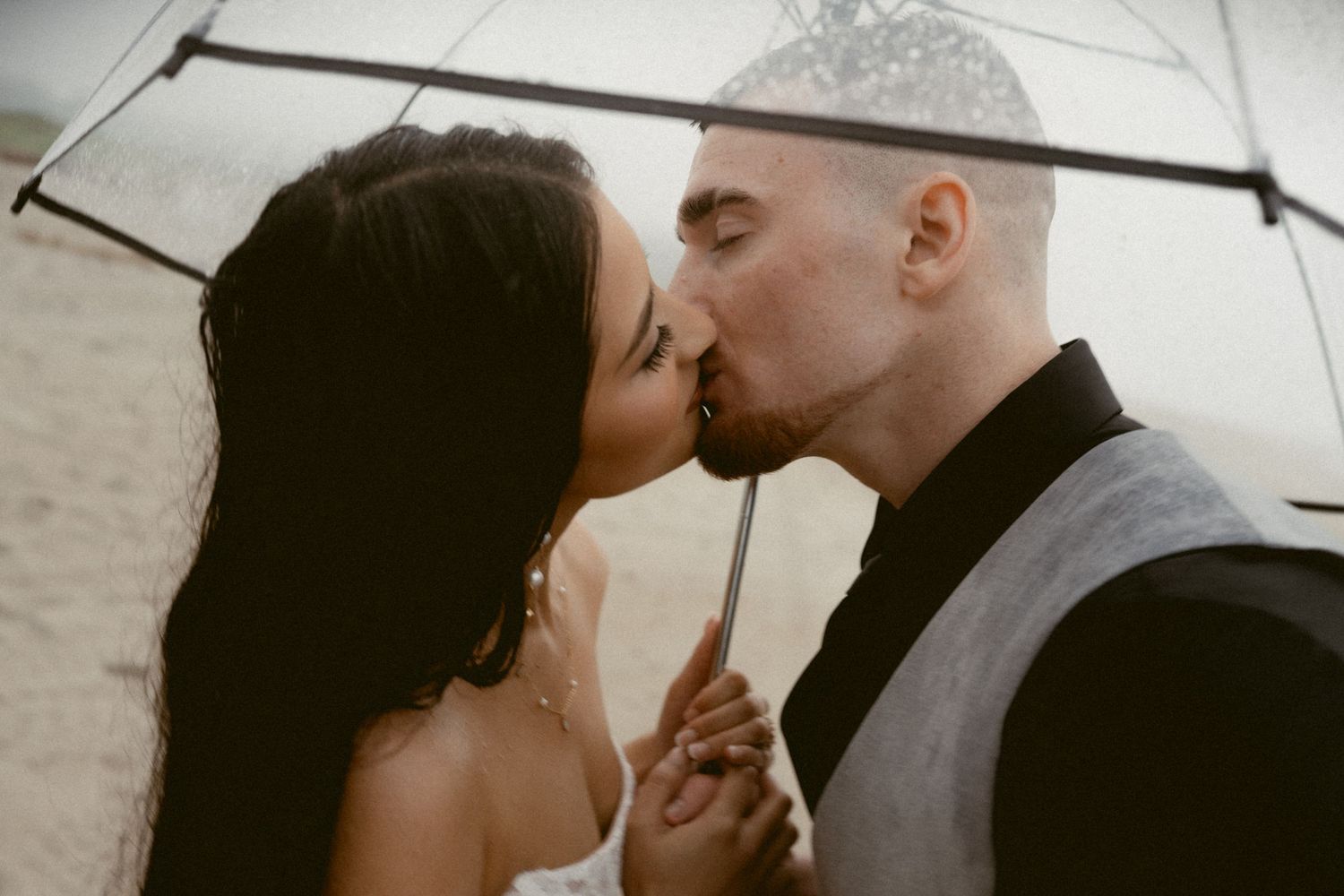 A romantic moment captured under an umbrella on a cloudy beach day.