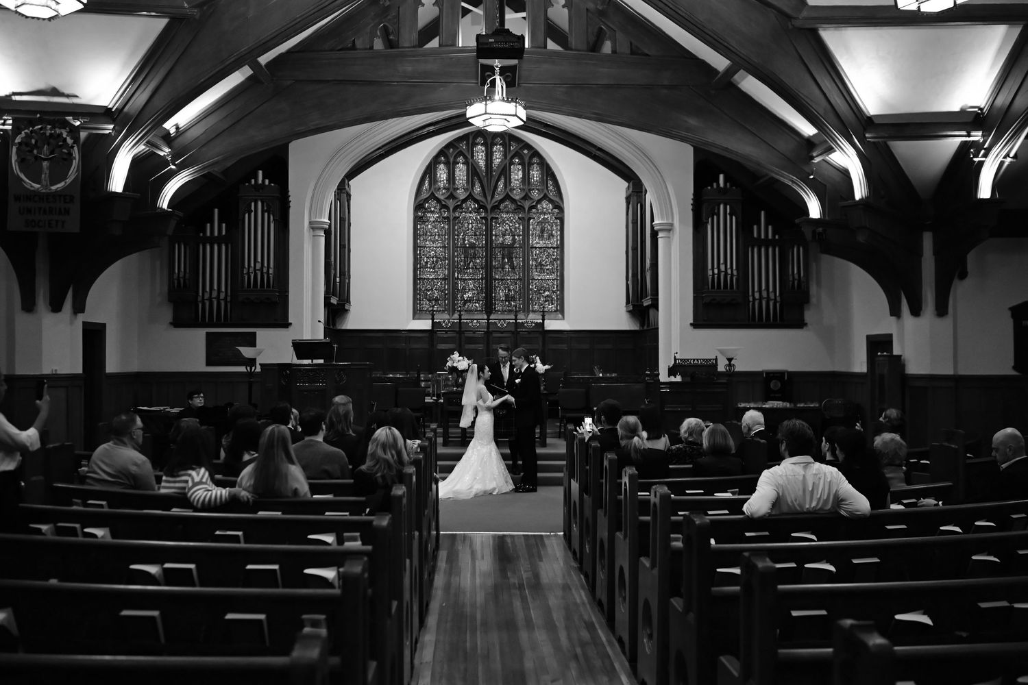 Wide angle view of church interior during wedding ceremony showing vaulted ceiling and pews.