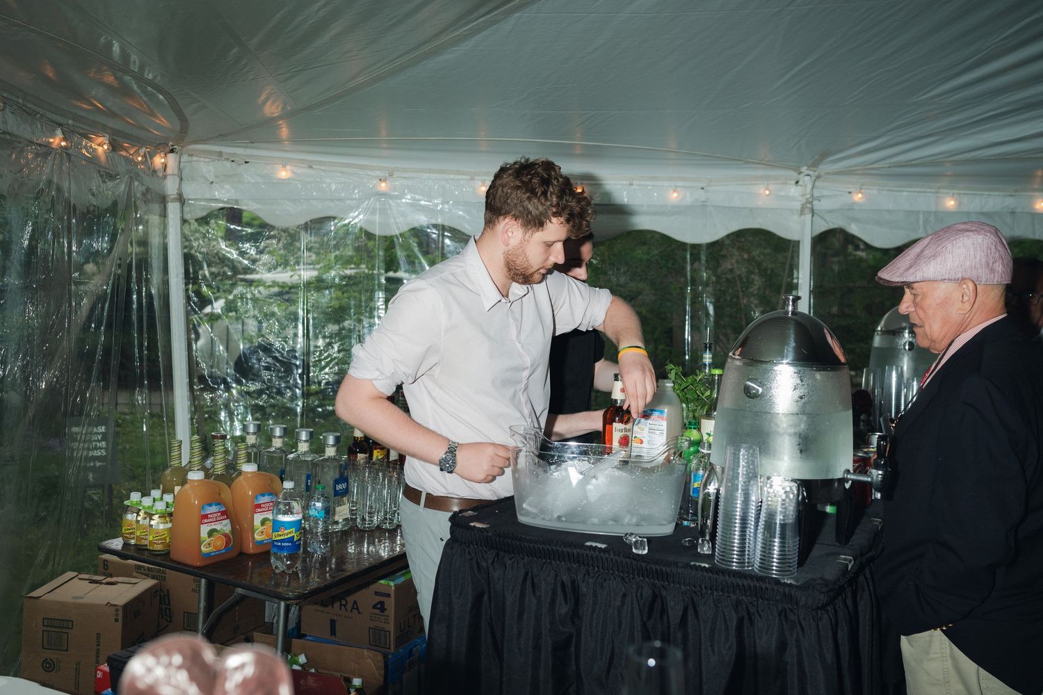 A bartender serving drinks at an outdoor wedding reception under a white tent.