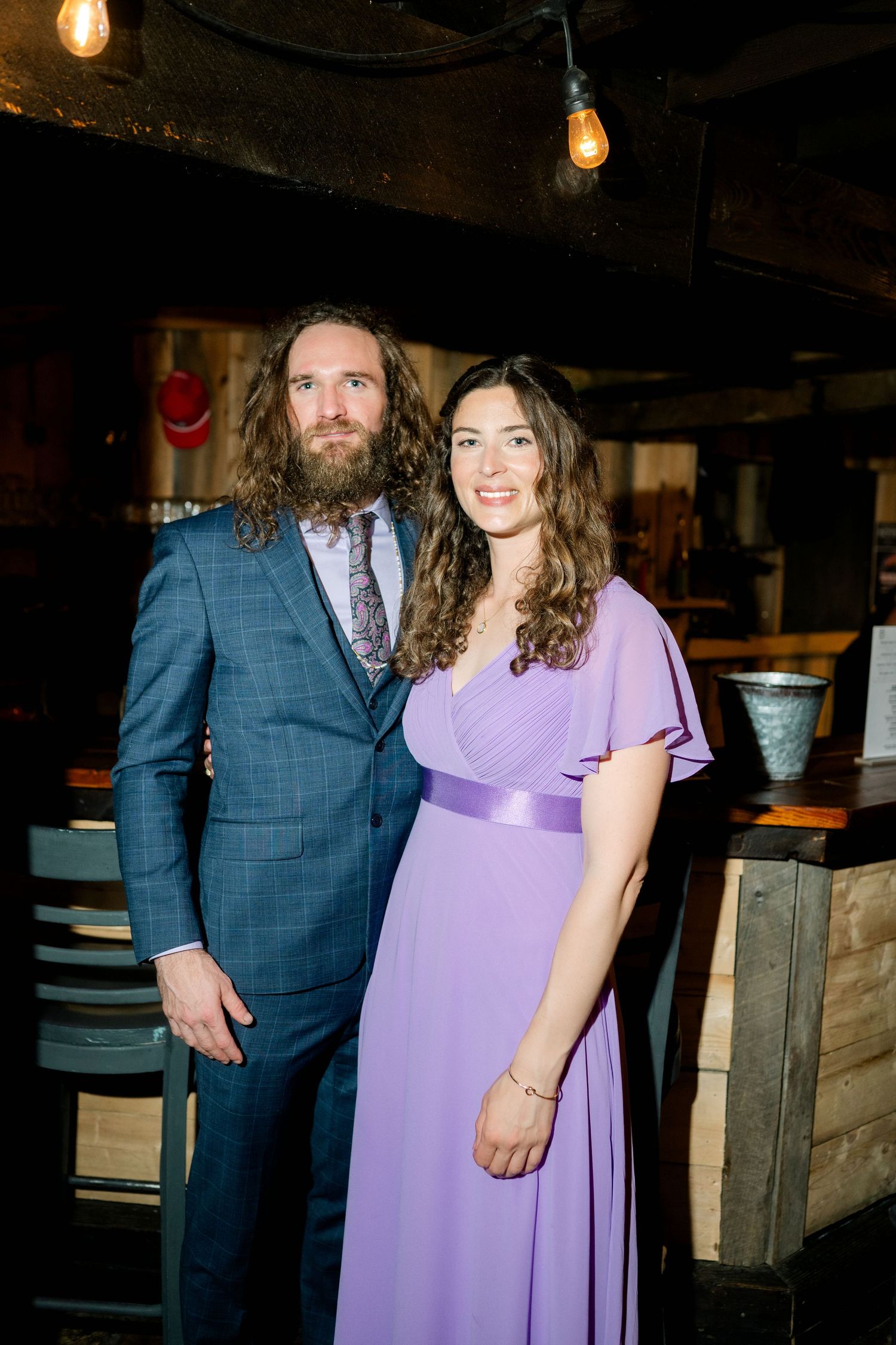 A couple poses together in a rustic venue with wooden details and ambient lighting.