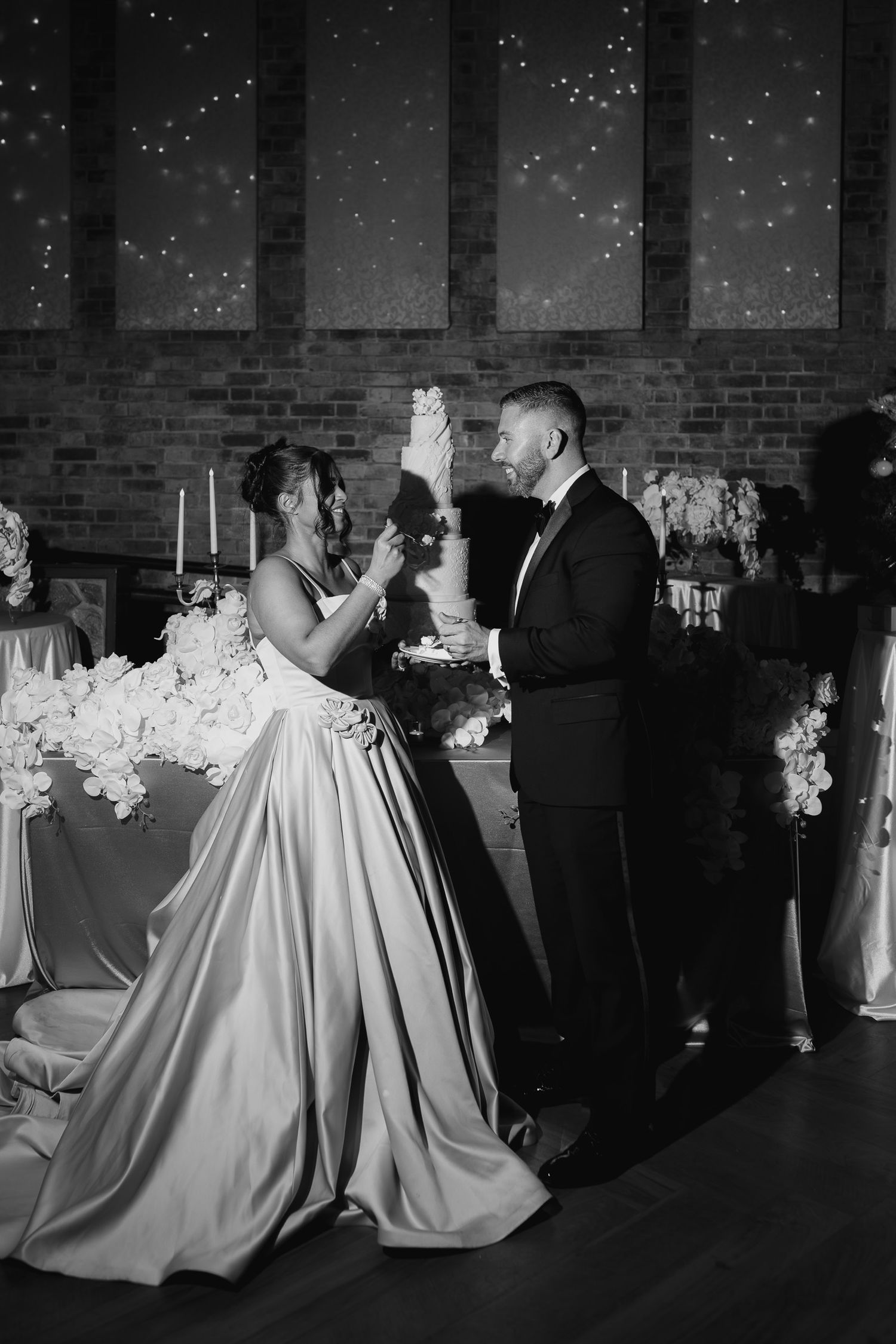 A bride in a satin ballgown and groom in a tuxedo share their first dance under twinkling lights at an elegant reception.