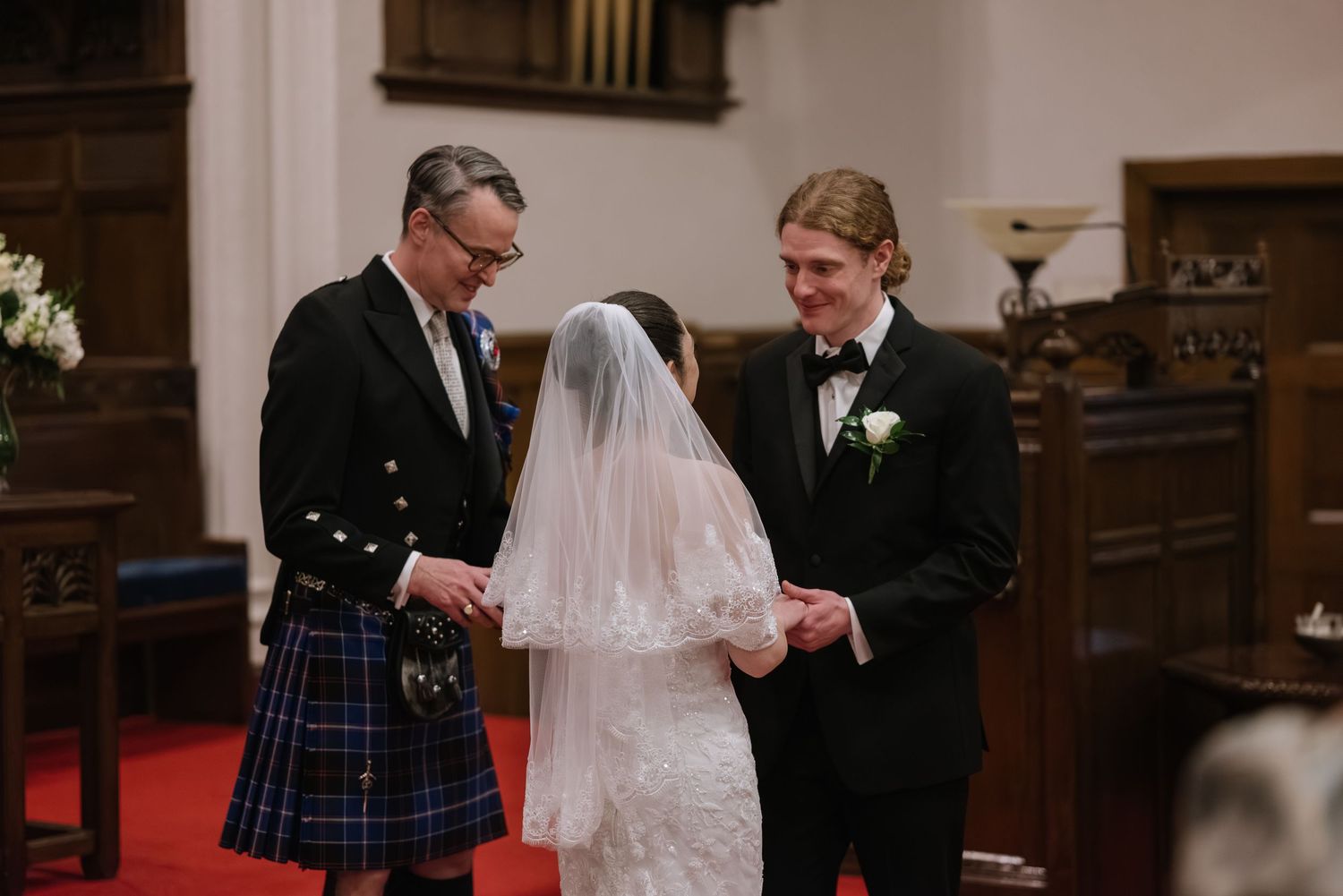 Wedding ceremony in a church with traditional Scottish kilts and formal attire.