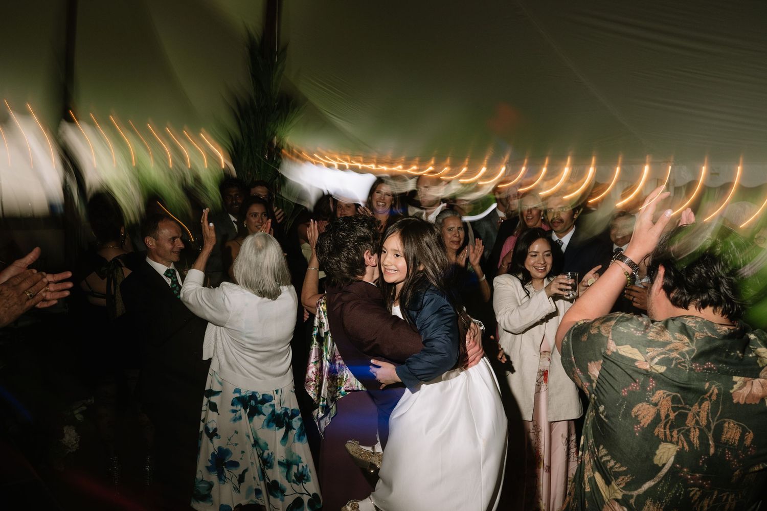 Guests dancing and embracing joyfully under warm string lights at an elegant wedding reception.