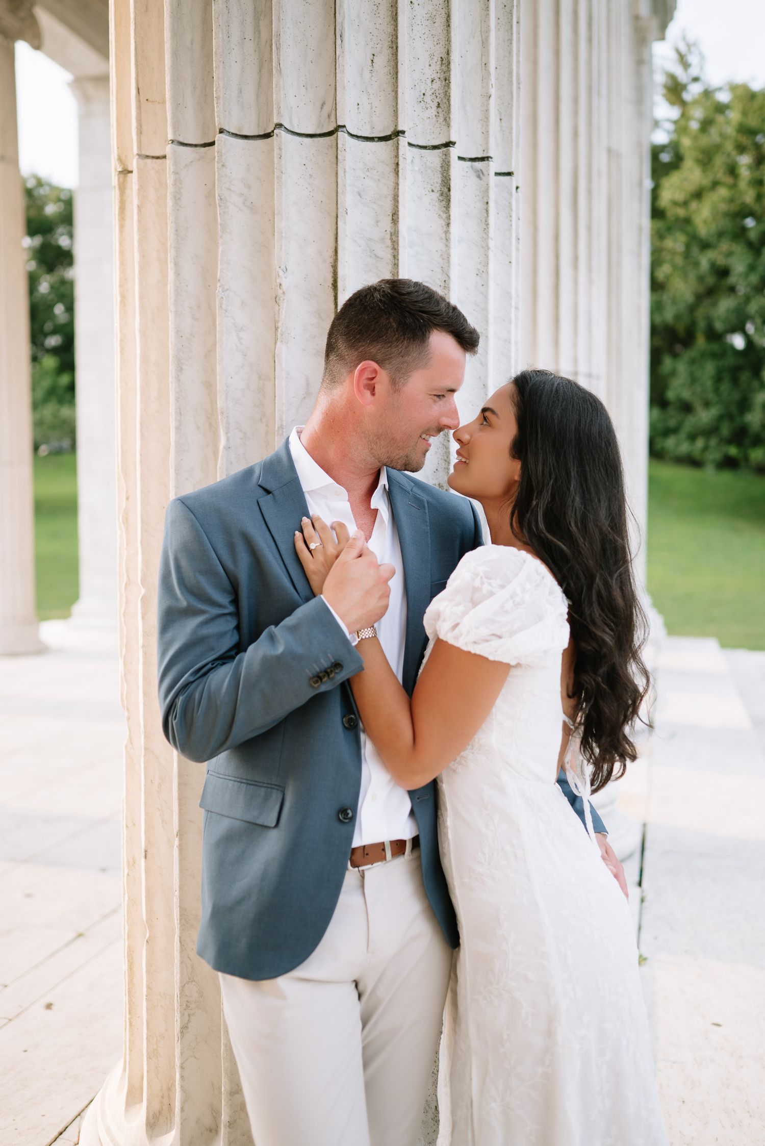 Couple shares intimate moments between classical white columns during outdoor photoshoot.