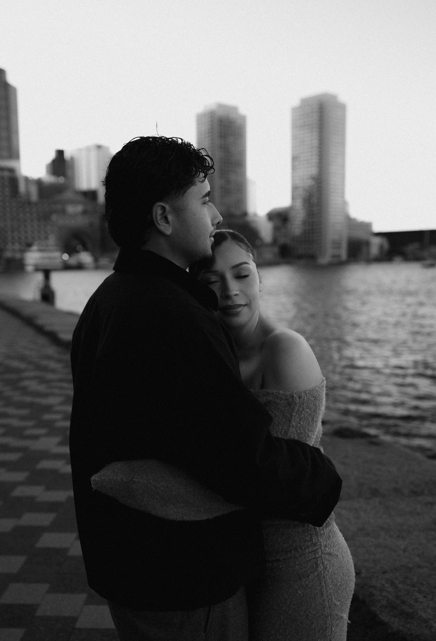 Urban waterfront engagement photo with city skyline in the background.
