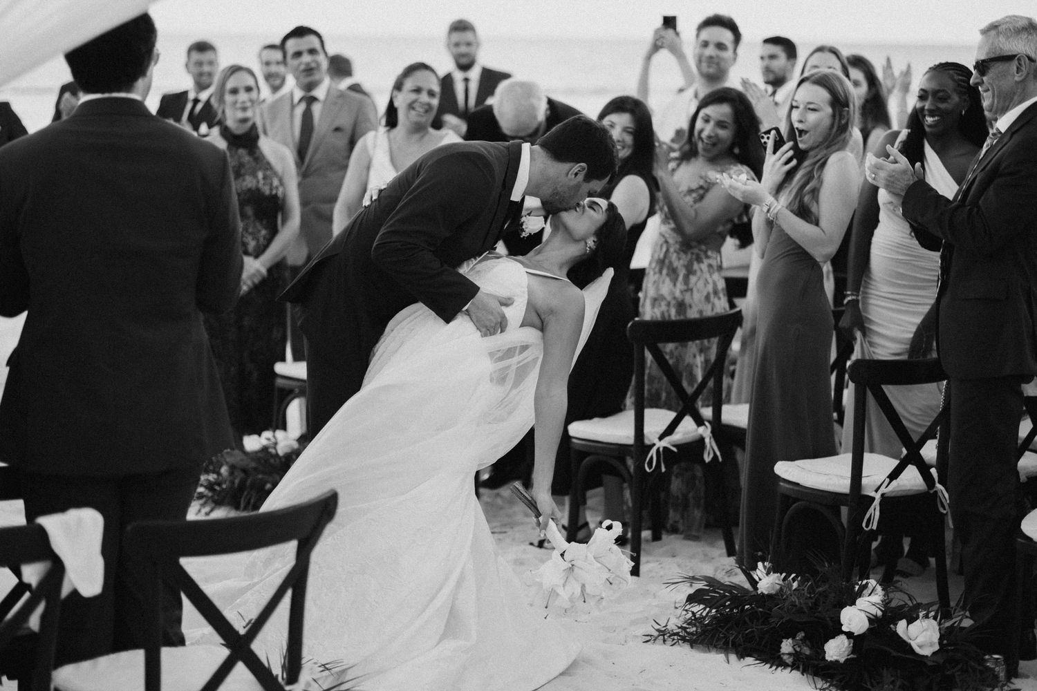 Wedding reception guests celebrate under a white tent with black cross-back chairs.
