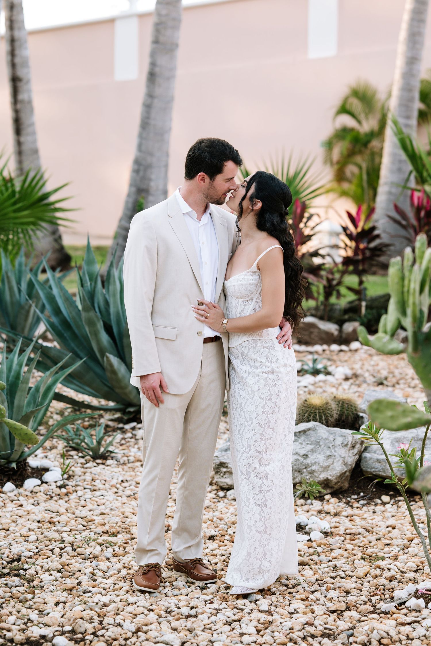 A romantic couple shares an intimate moment in a tropical garden setting with palm trees and decorative stones.
