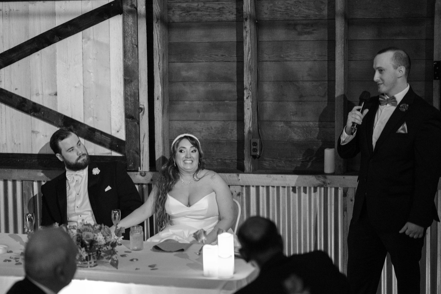 A rustic barn wedding reception with guests seated at long tables and ambient lighting.