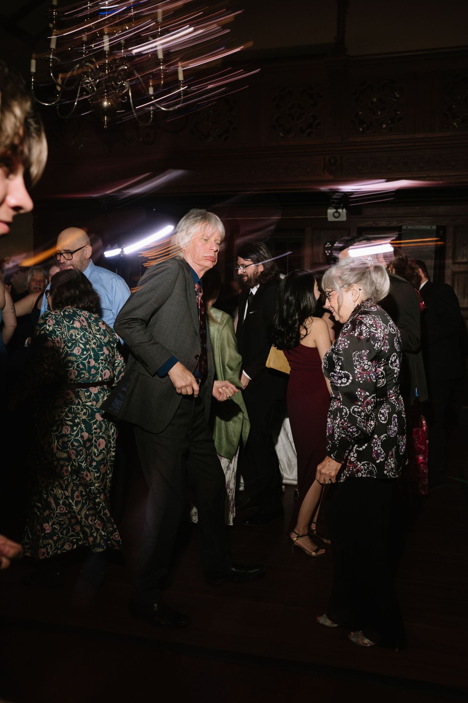 Wedding guests dancing together on a dimly lit dance floor during a lively wedding reception celebration.