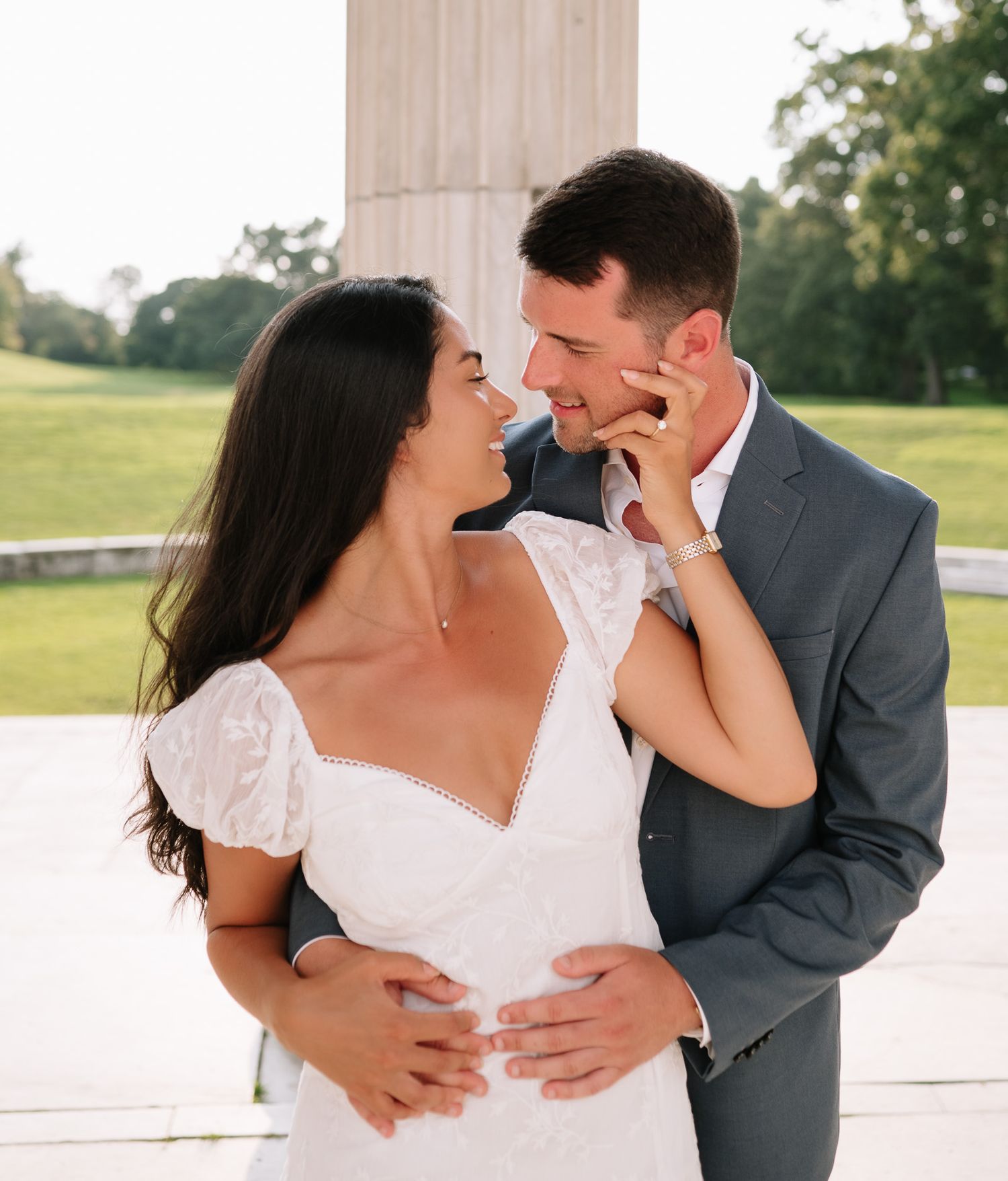 A romantic couple in white and gray formal wear share intimate moments on a stone terrace.