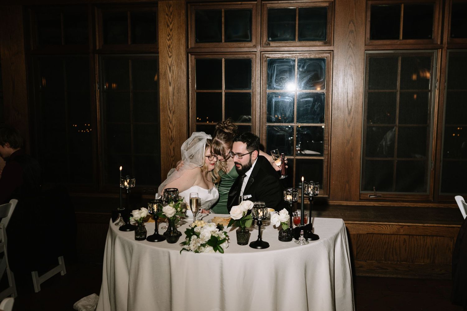 Bride and groom sit closely together at candlelit sweetheart table with white floral arrangements.