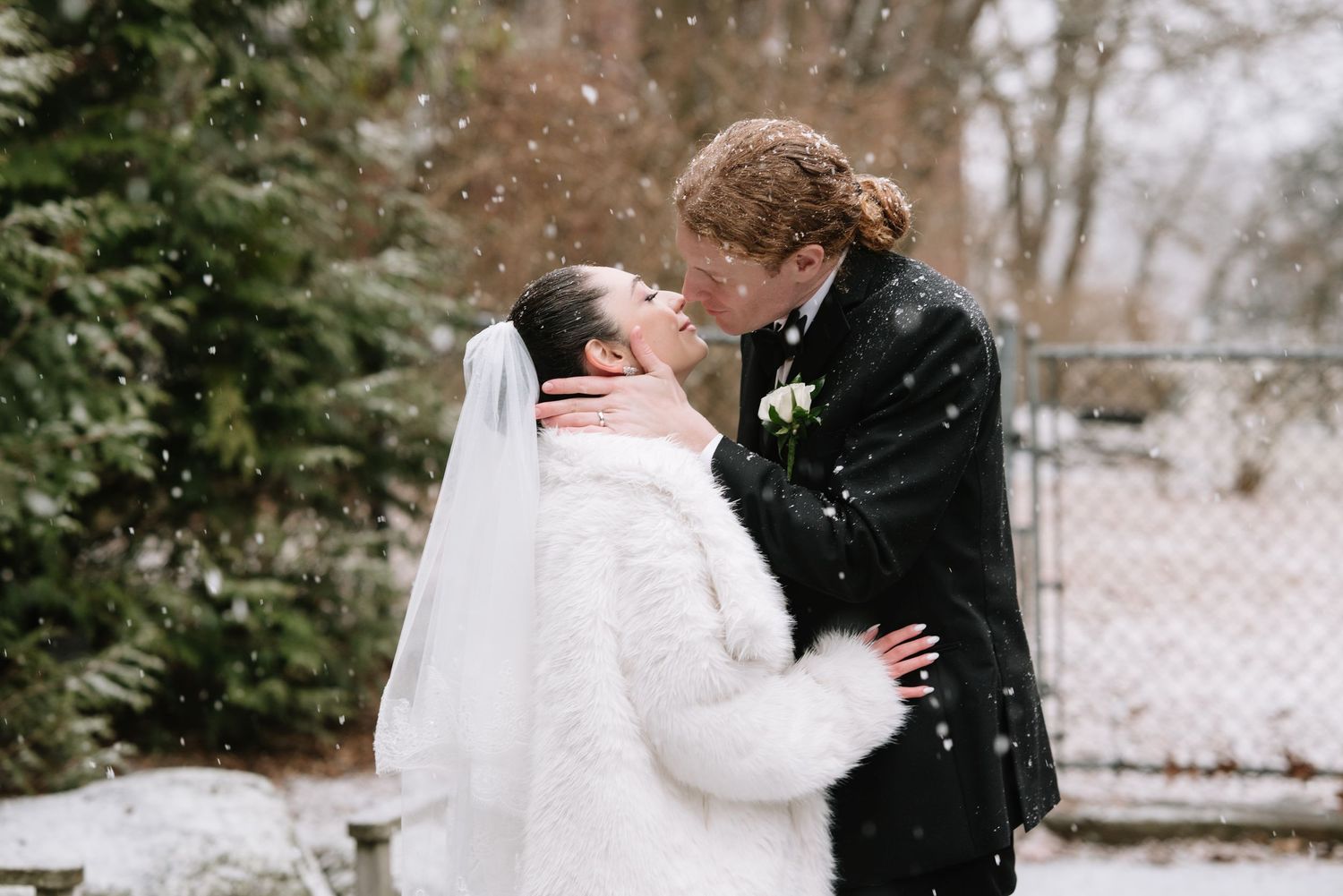 Winter wedding couple embracing in the snow with evergreen trees in the background.