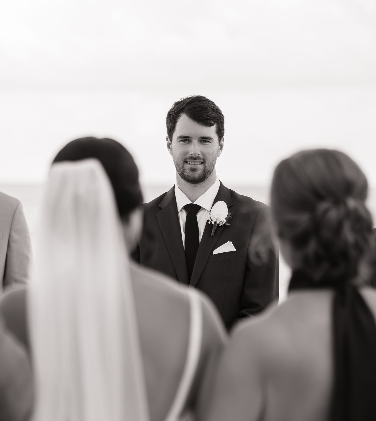A black and white wedding photograph showing a couple during their ceremony with guests in the background.