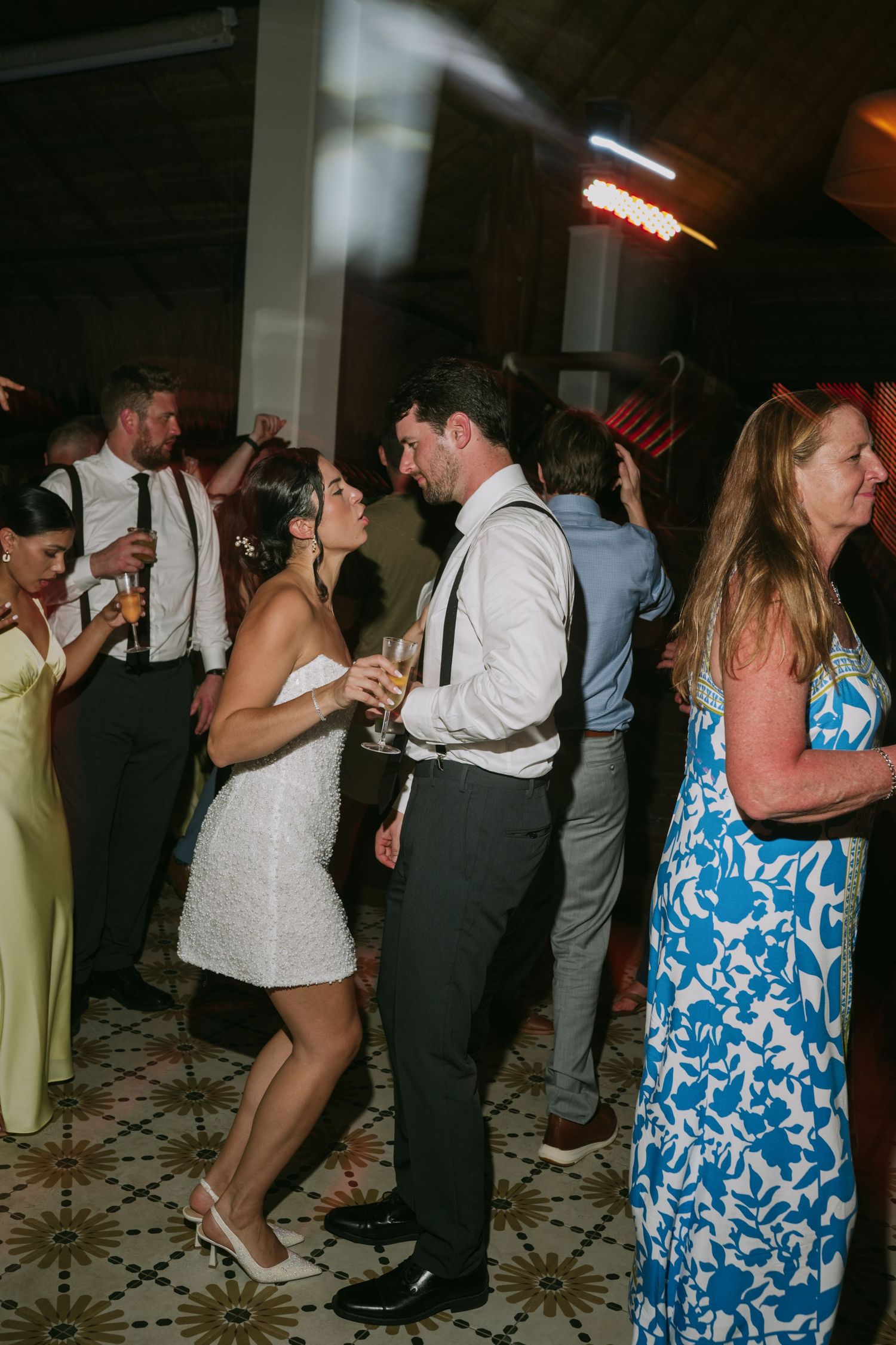 Wedding guests dancing in formal attire and summer dresses at an evening reception.