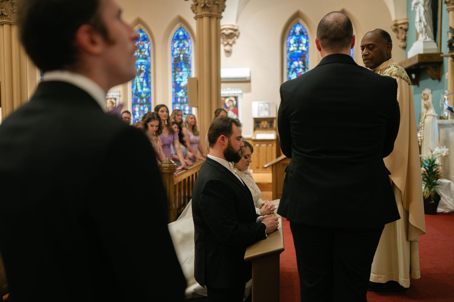 Church interior with stained glass windows and wooden pews during a wedding ceremony.