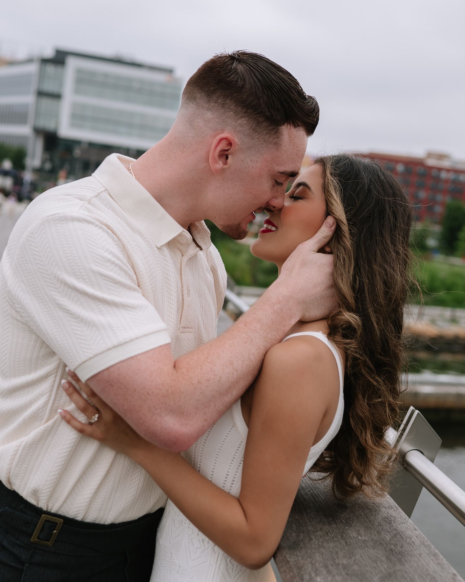 Couple sharing intimate moments on urban waterfront with skyline views.