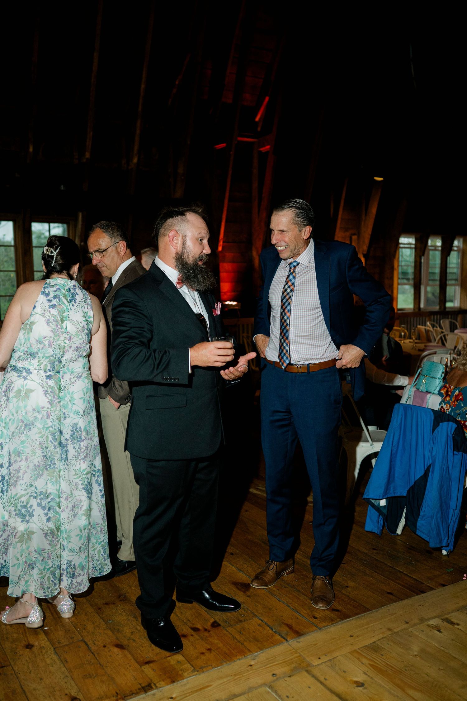 Wedding guests dancing in formal attire on a wooden dance floor at an evening reception.
