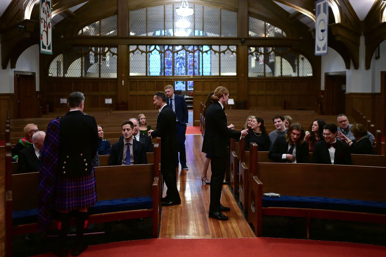 Wedding ceremony taking place in a traditional church sanctuary with wooden pews and stained glass windows.