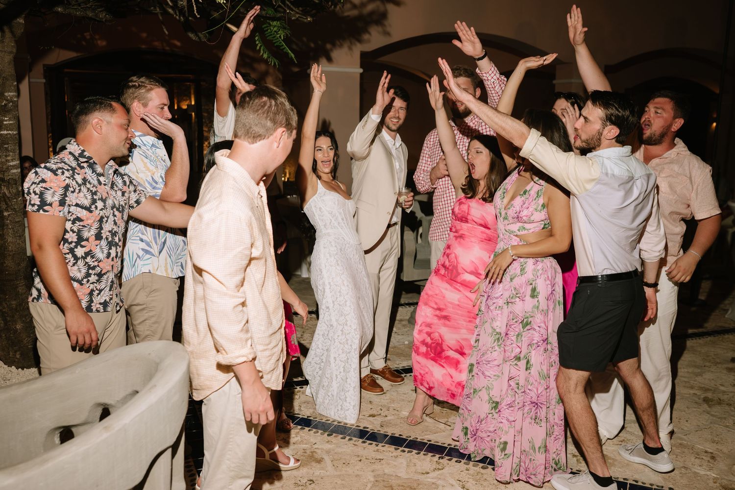 Guests dancing together in a joyful celebration with people wearing pink and white outfits.