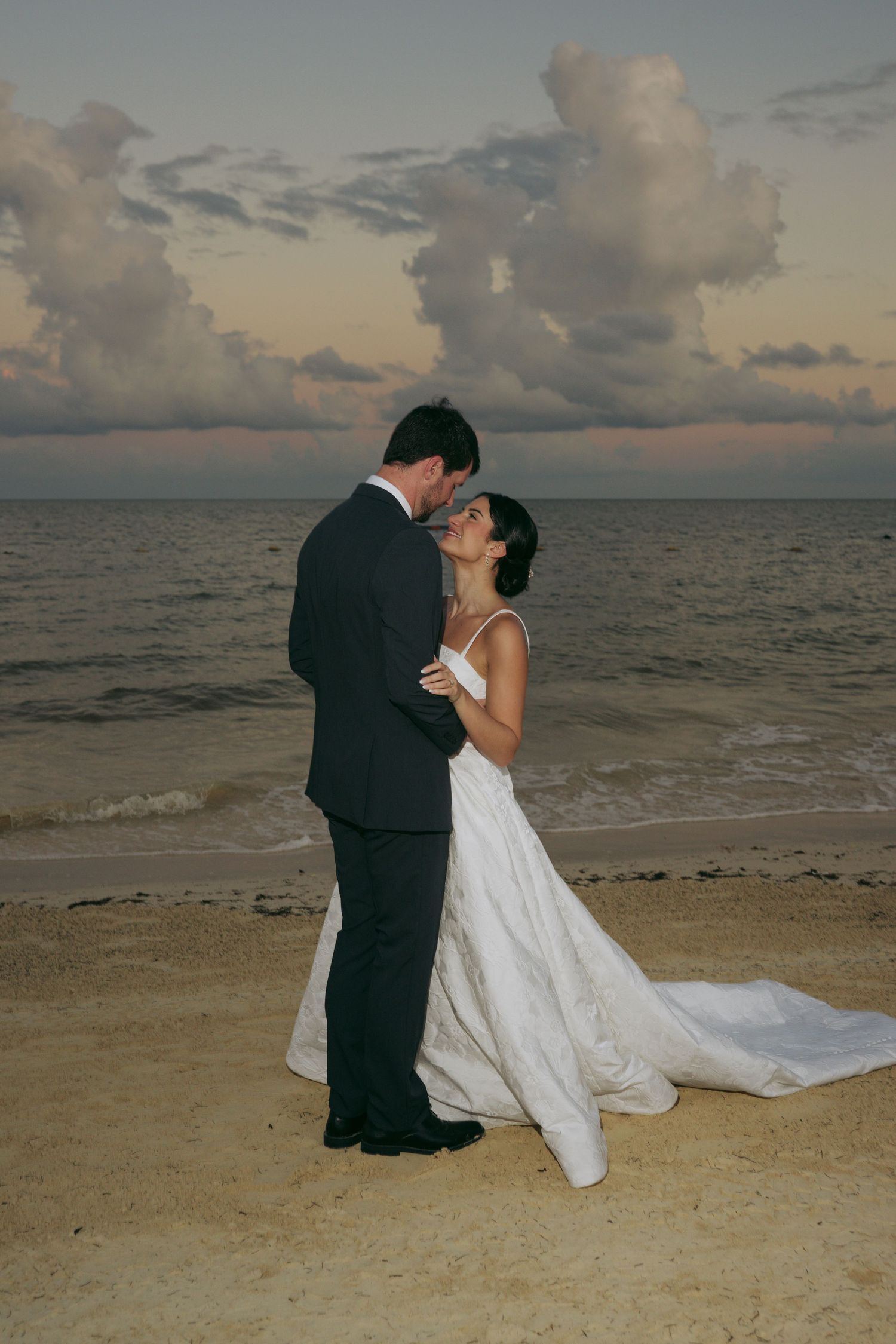 A romantic beach wedding photoshoot at sunset with a couple embracing on the sandy shore.