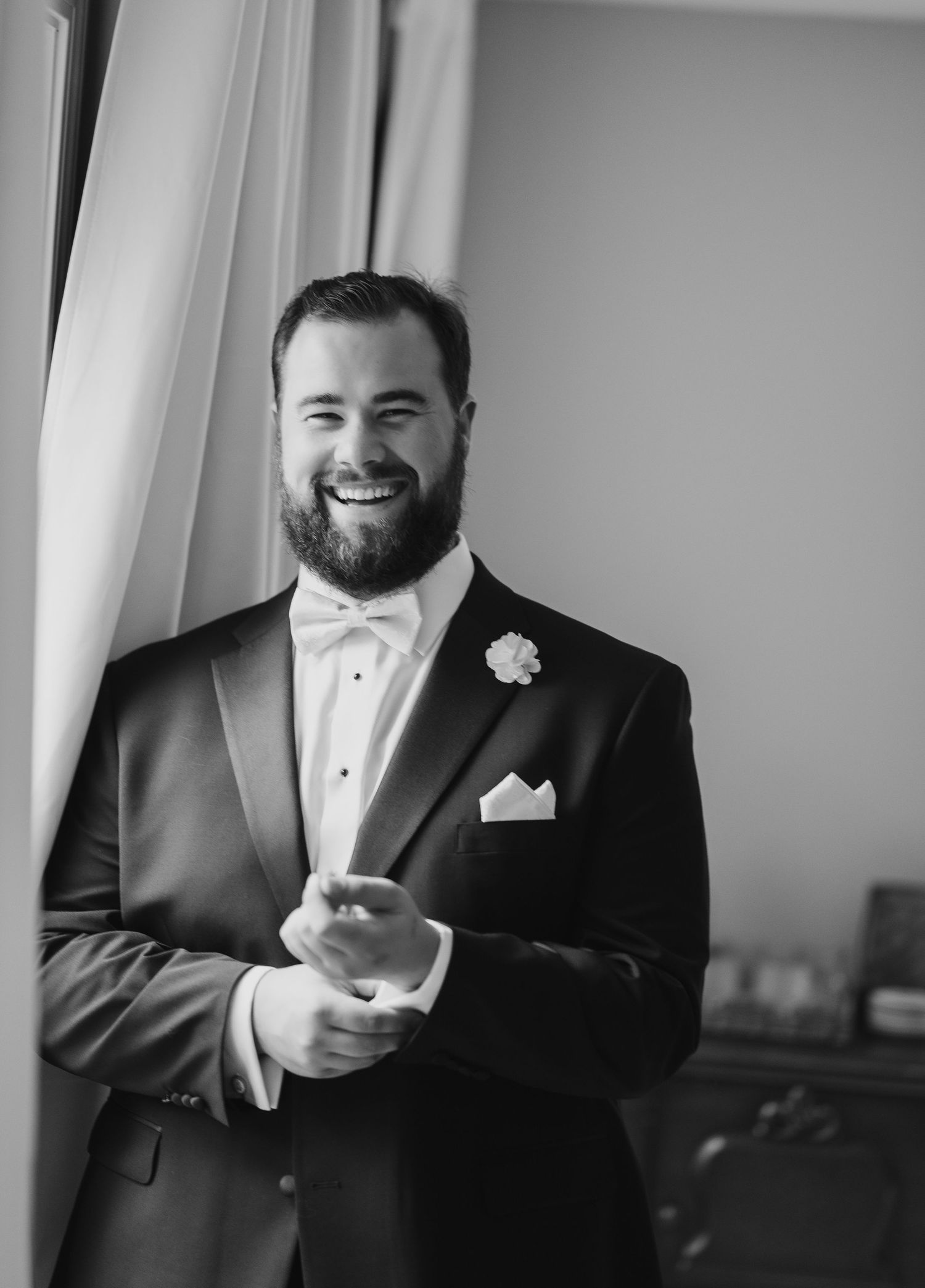 Black and white photo of a groom in formal attire with white bow tie and pocket square.