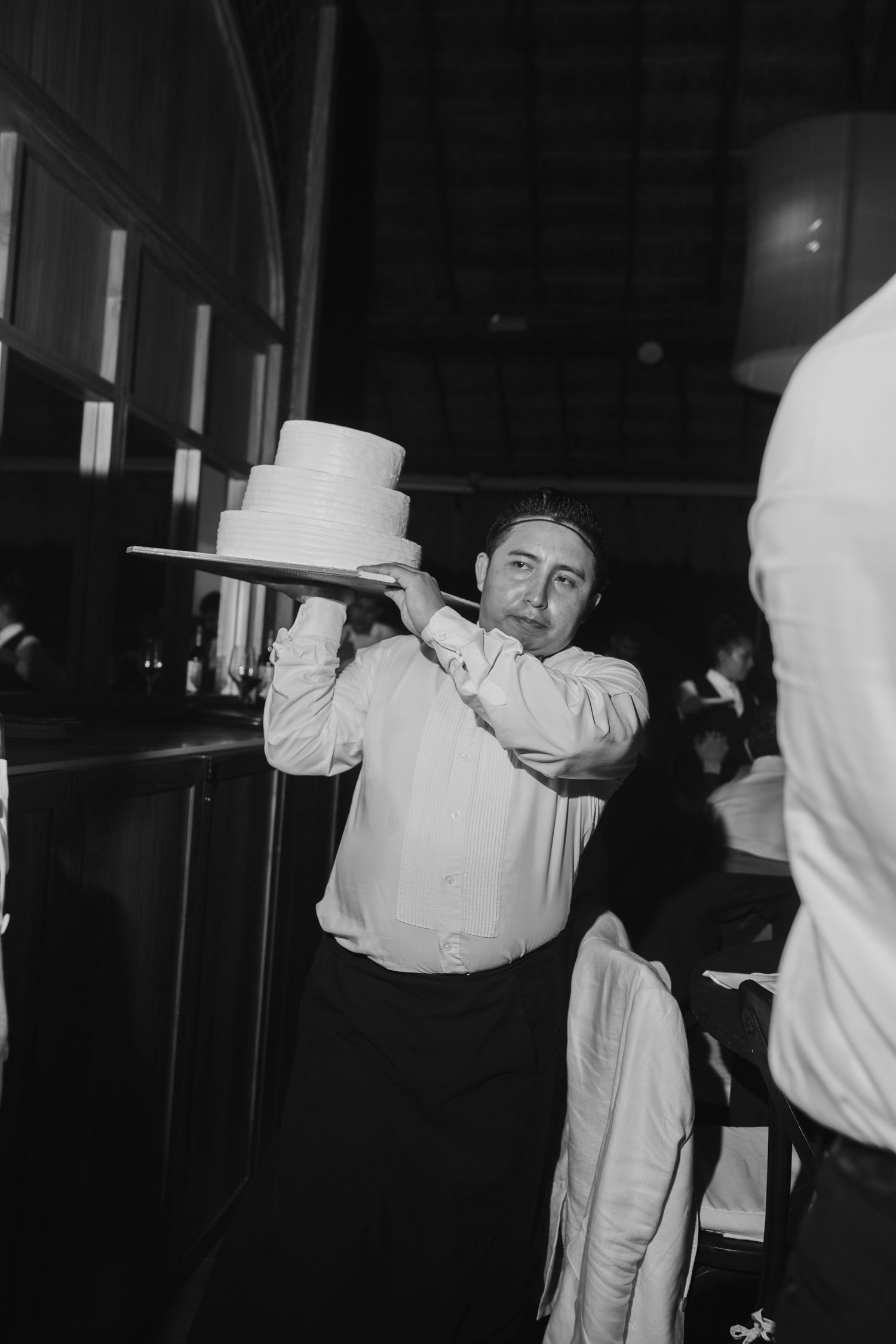 Servers in white uniforms carry plates through a darkened reception venue.