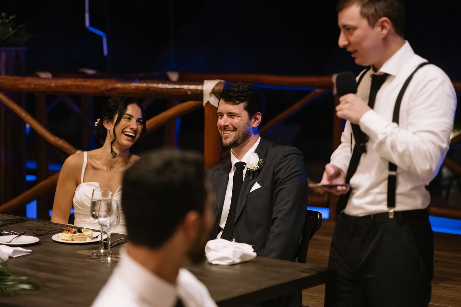 Wedding reception guests share laughter and conversation at a dimly lit table.