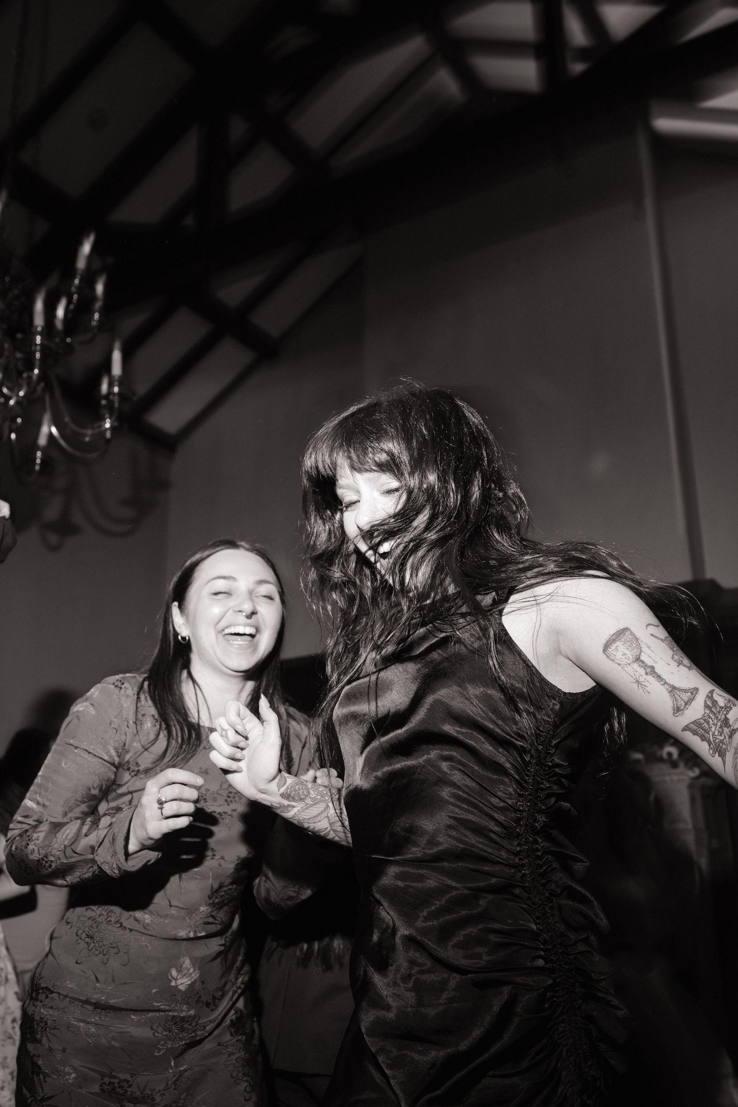 Two women laugh and dance together in black and white photo at a lively indoor celebration event.