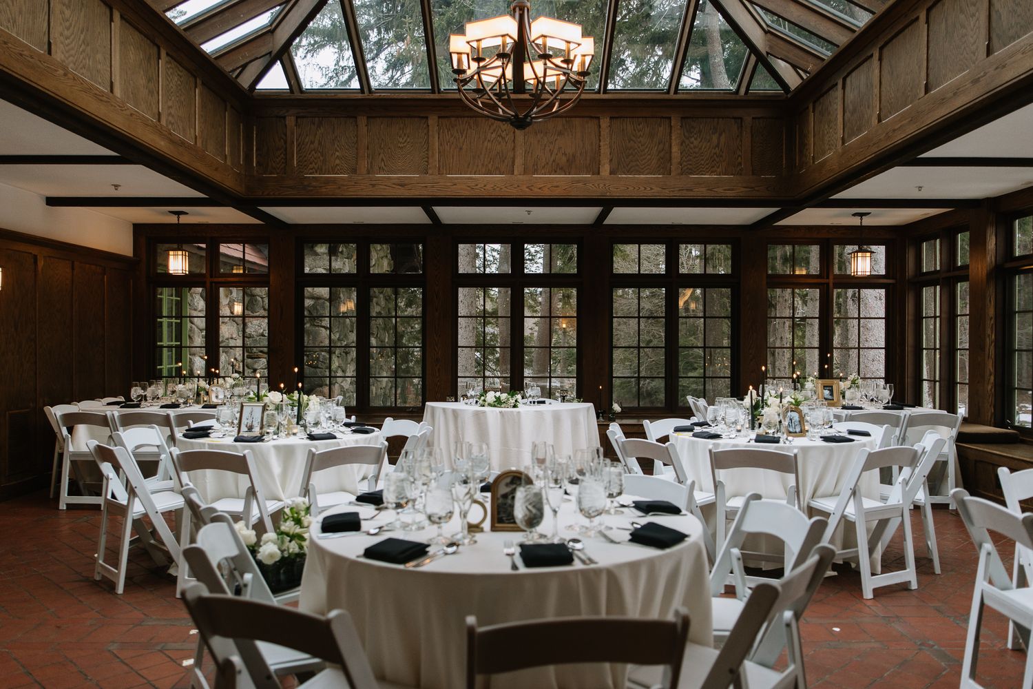 Elegant wedding reception hall with round tables, white linens, and a glass ceiling conservatory venue.