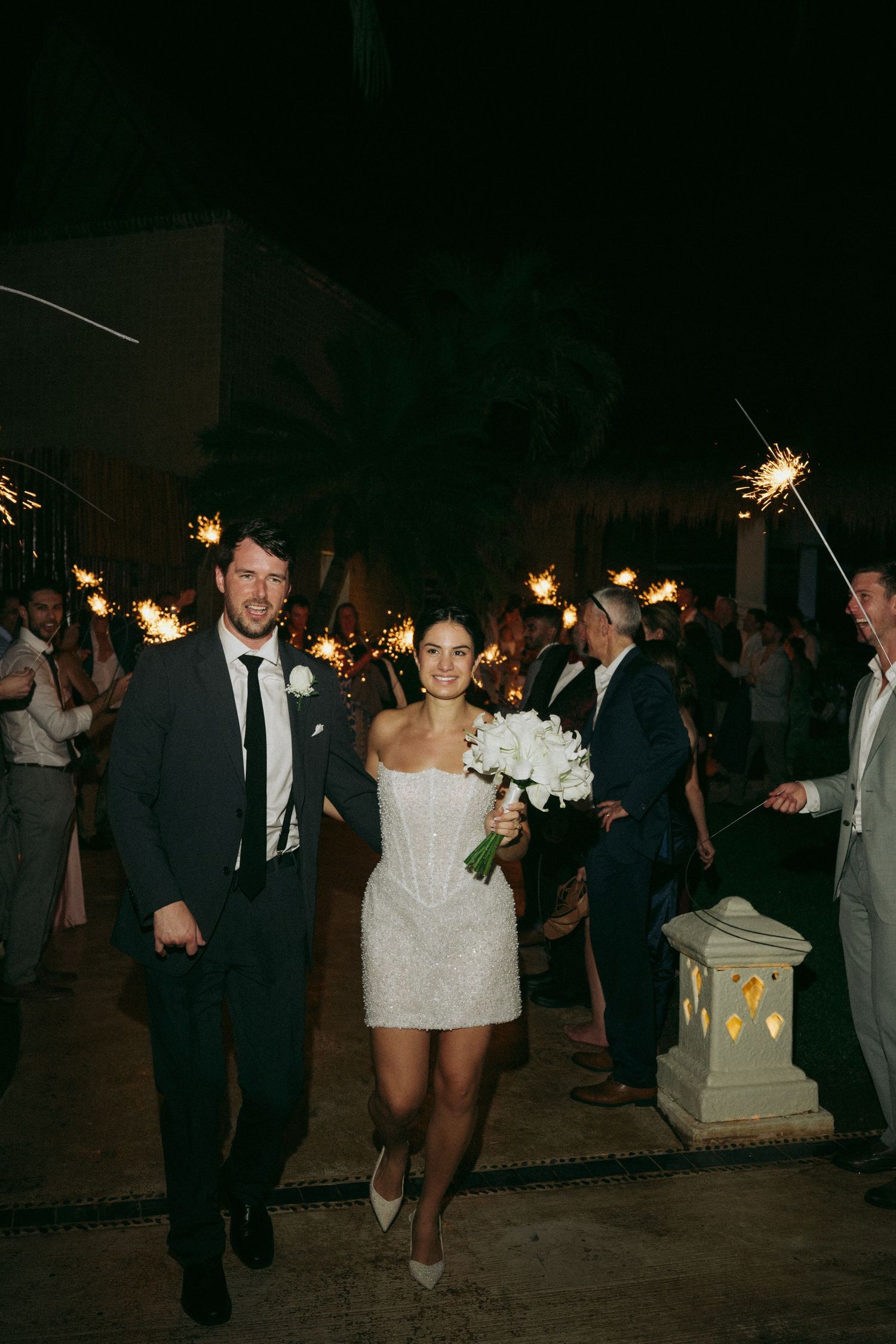 Wedding party members walk with sparklers creating a magical nighttime exit scene.