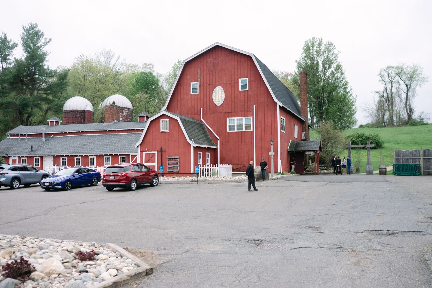 Red barn wedding venue with classic cars parked outside on a sunny spring day.