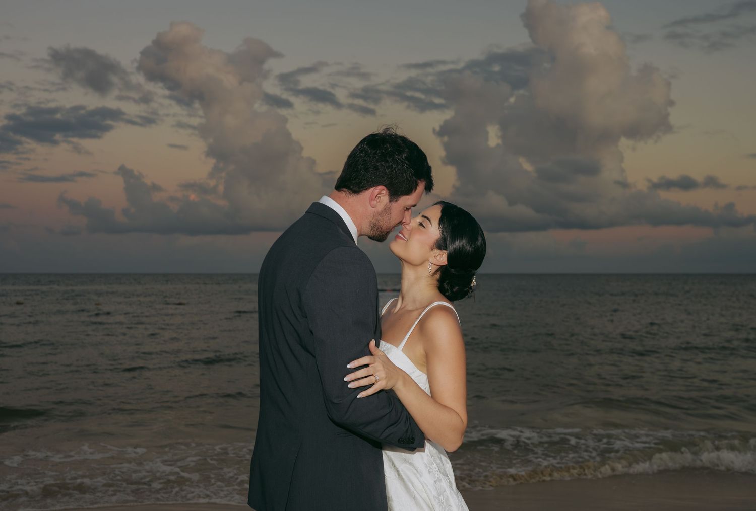 A romantic beach wedding photo series shows a couple embracing at sunset with ocean waves and clouds in the background.