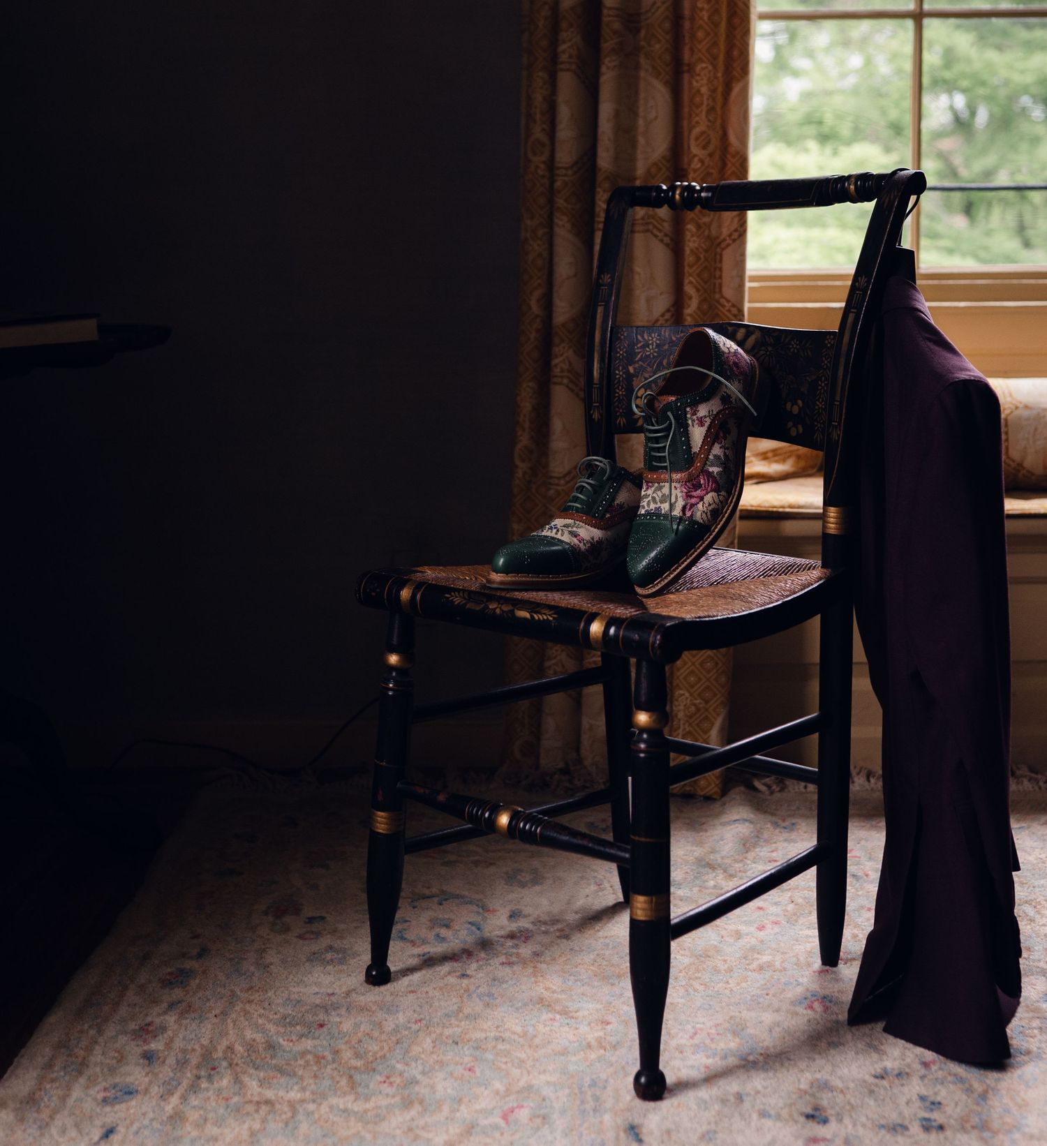 Vintage black chair with colorful cowboy boots and draped purple fabric near a curtained window.