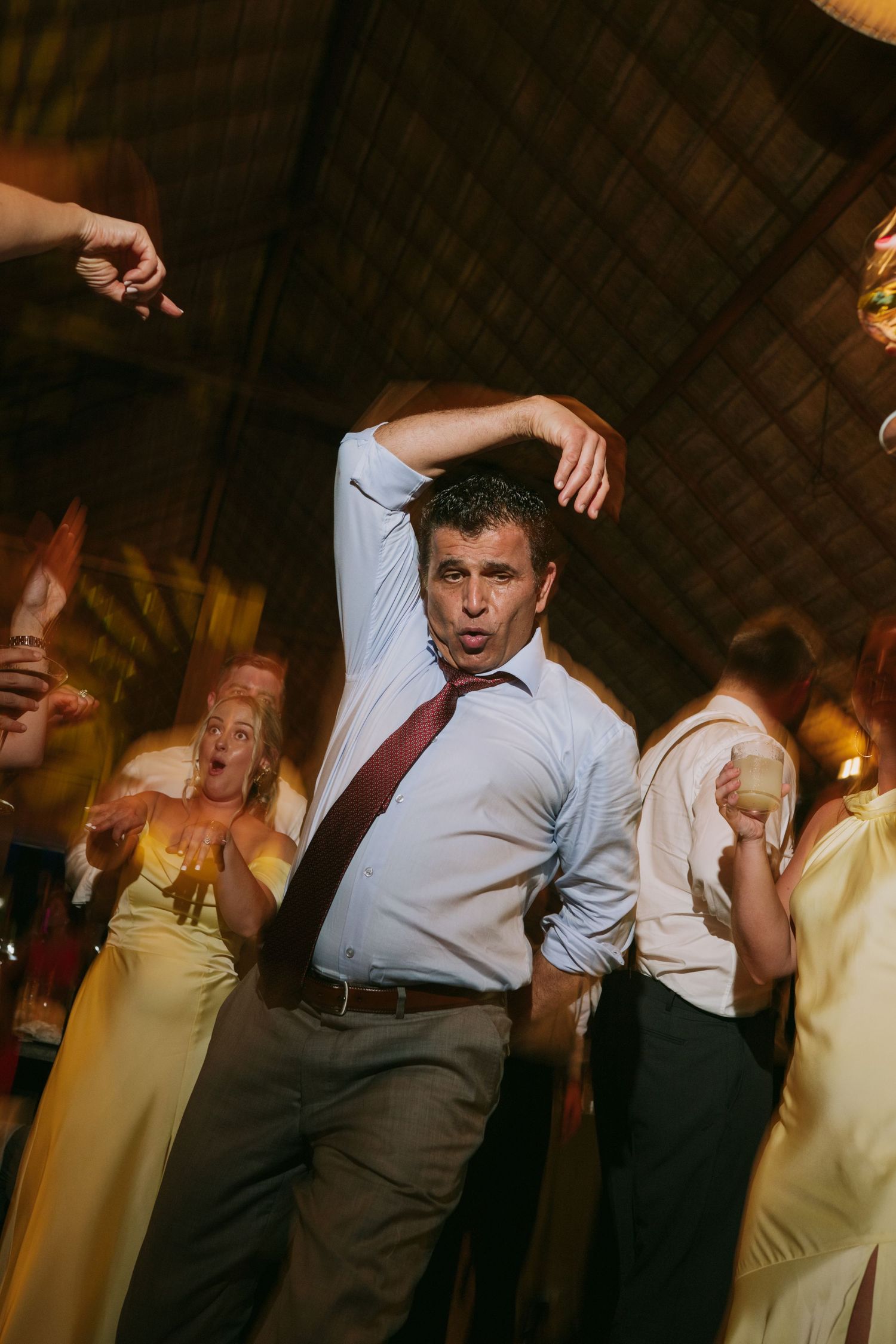 People dancing and celebrating energetically at a dimly lit indoor wedding reception.