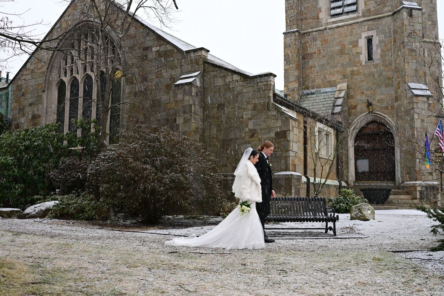 Stone church exterior with snow-covered grounds and winter trees against an overcast sky.