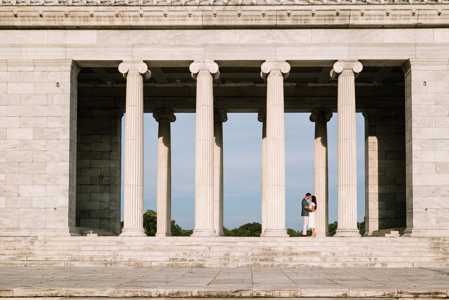 Classical white stone columns create an architectural backdrop against a bright sky.