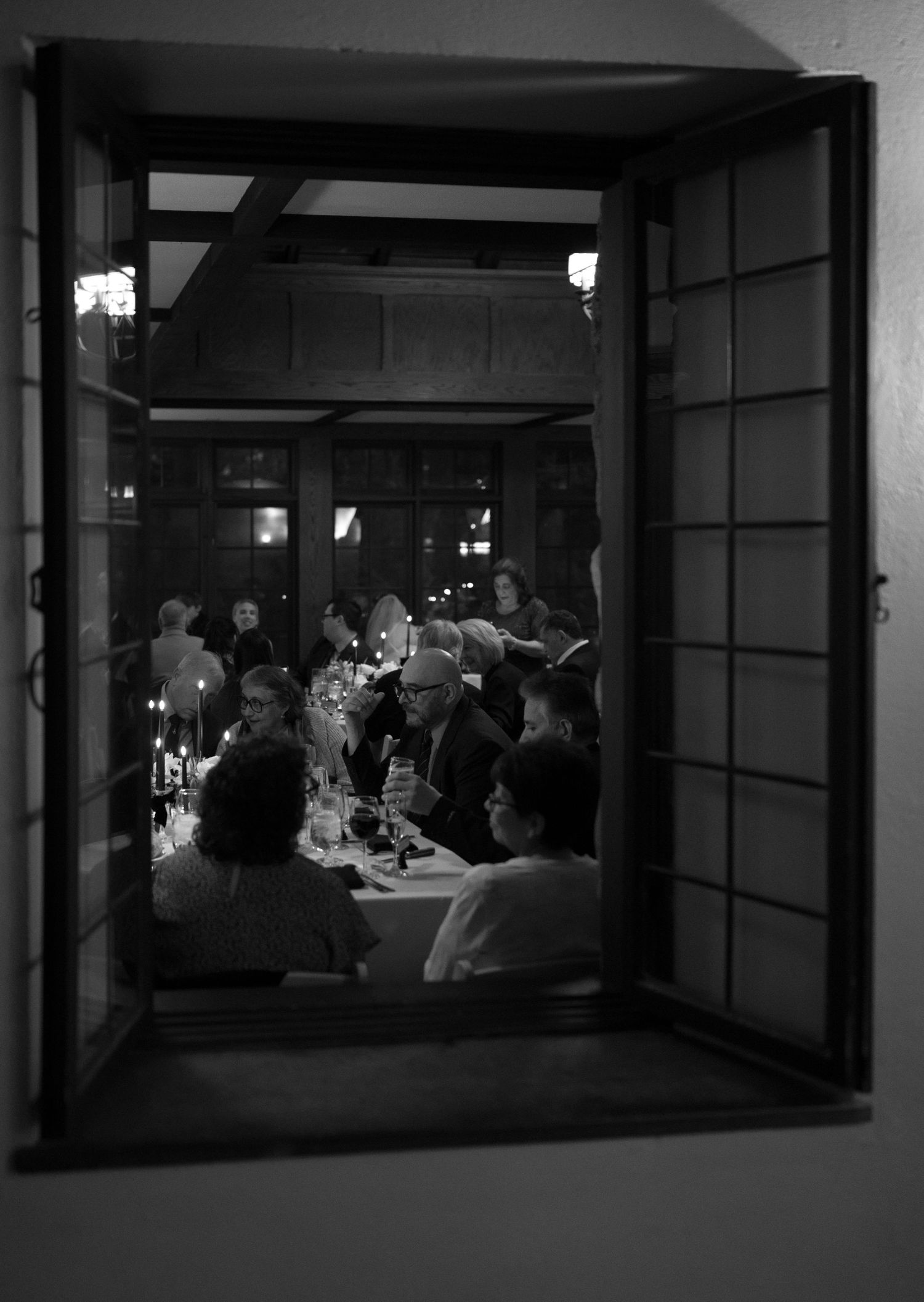 Black and white photo of wedding reception dinner guests viewed through an open Japanese-style window.