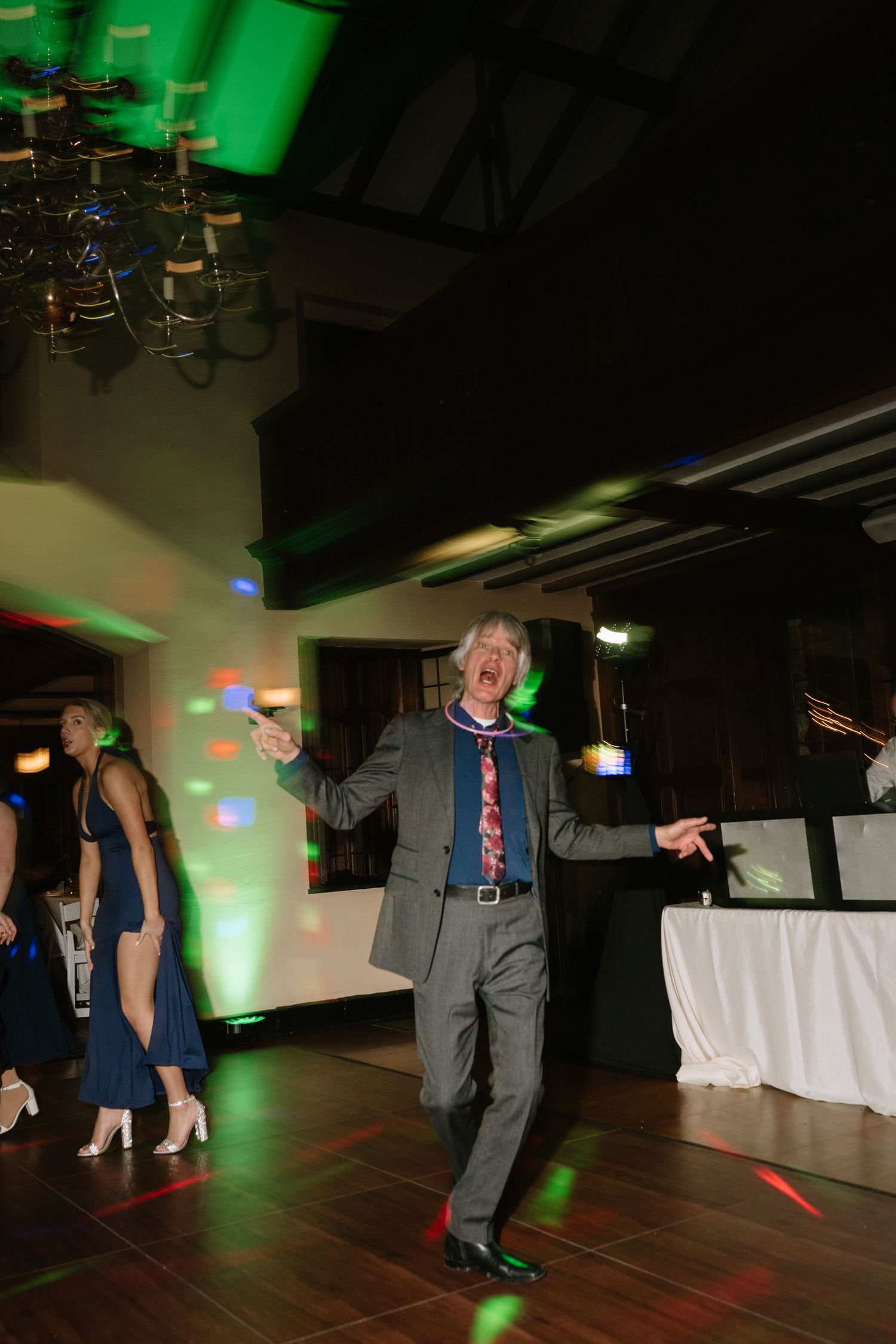 Energetic wedding guest dancing under colorful disco lights on the reception dance floor at night.
