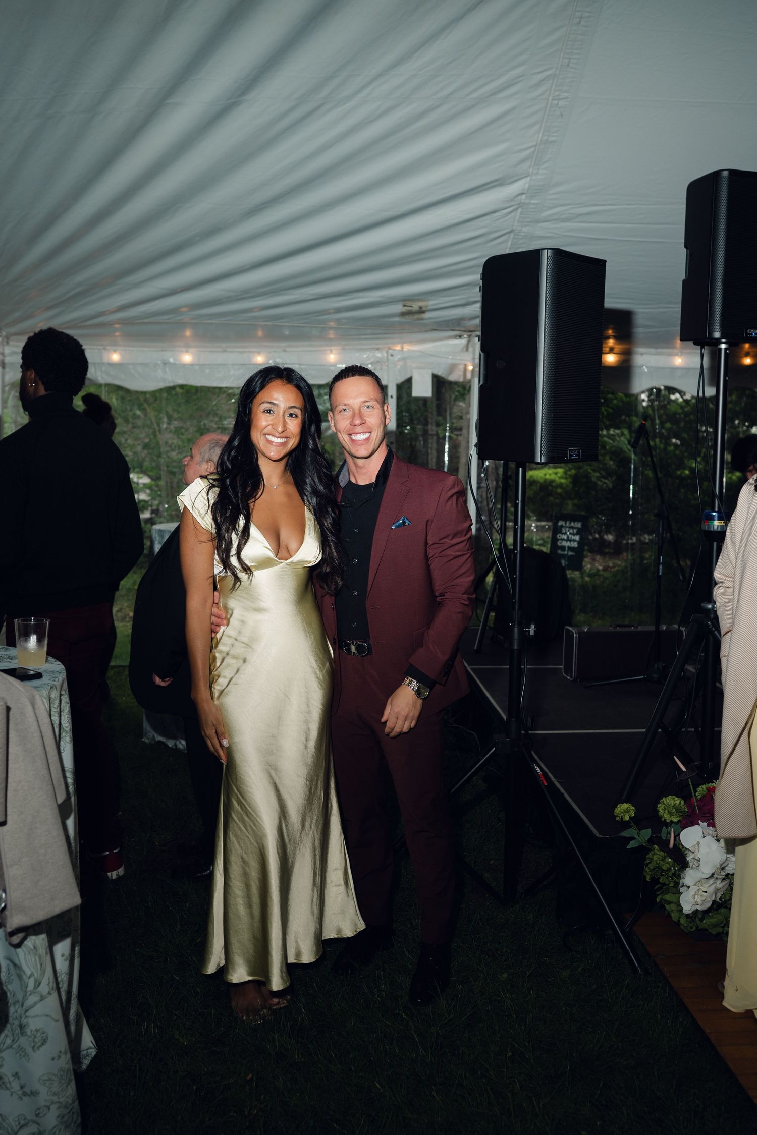 Couple posing together at an elegant outdoor wedding reception under a white tent.