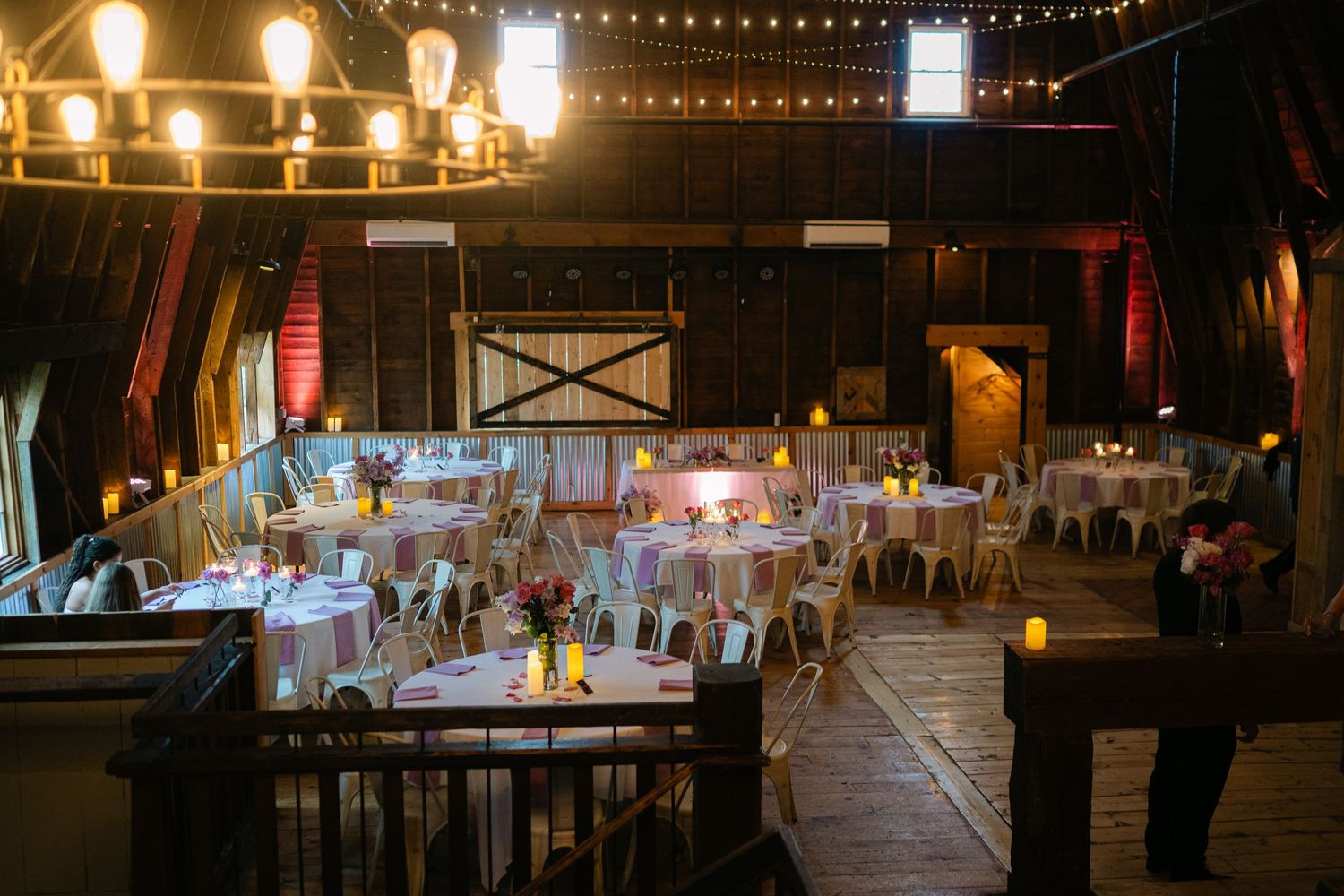 A rustic barn wedding venue decorated with string lights and table settings for an evening reception.