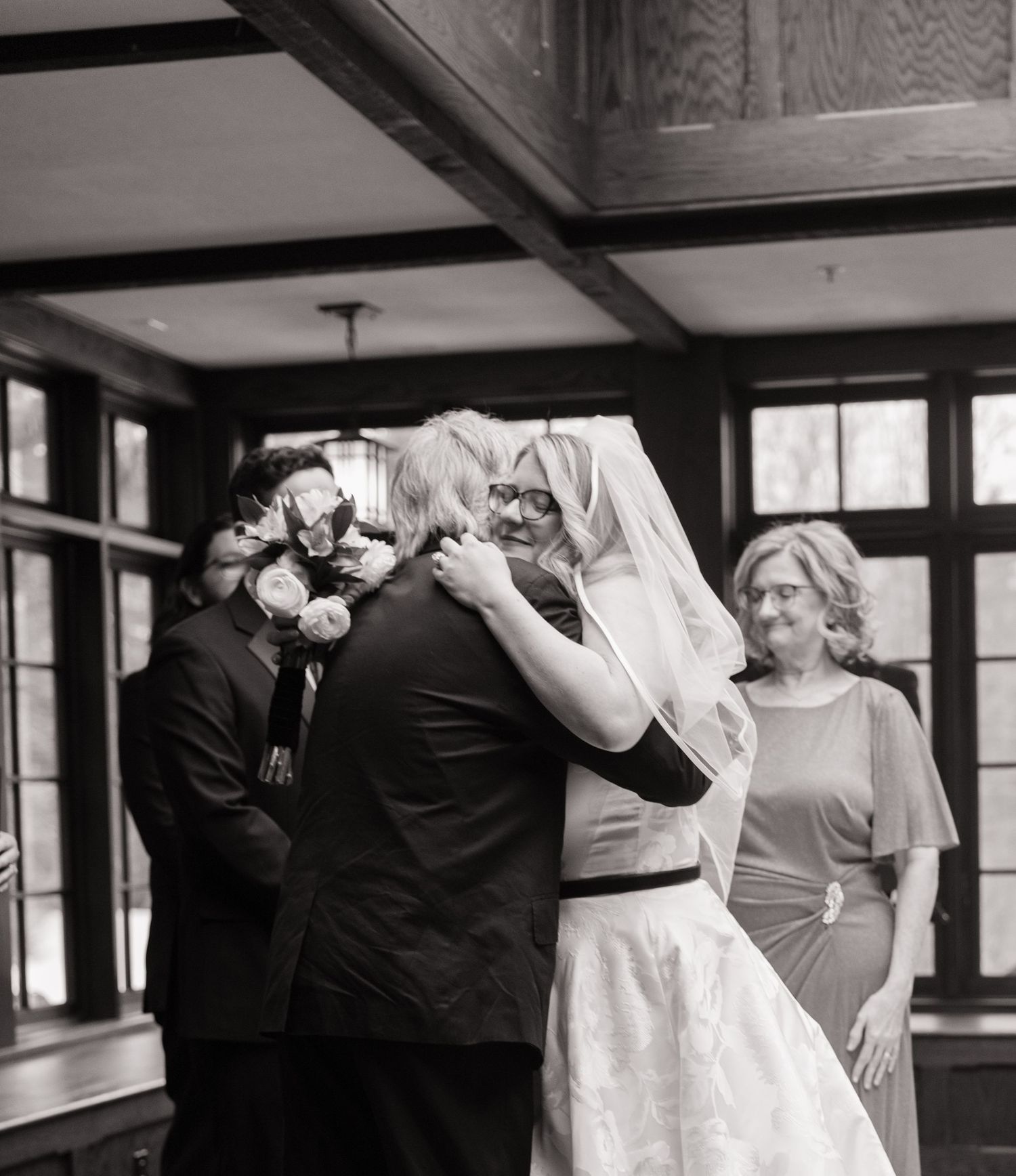 Black and white photo of a bride and groom sharing their first dance at a wedding reception indoors.