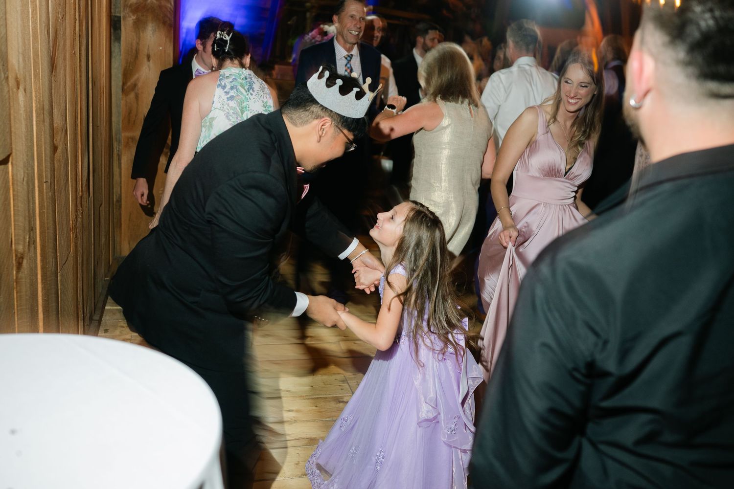 Wedding guests dancing and celebrating at an evening reception with blue lighting.