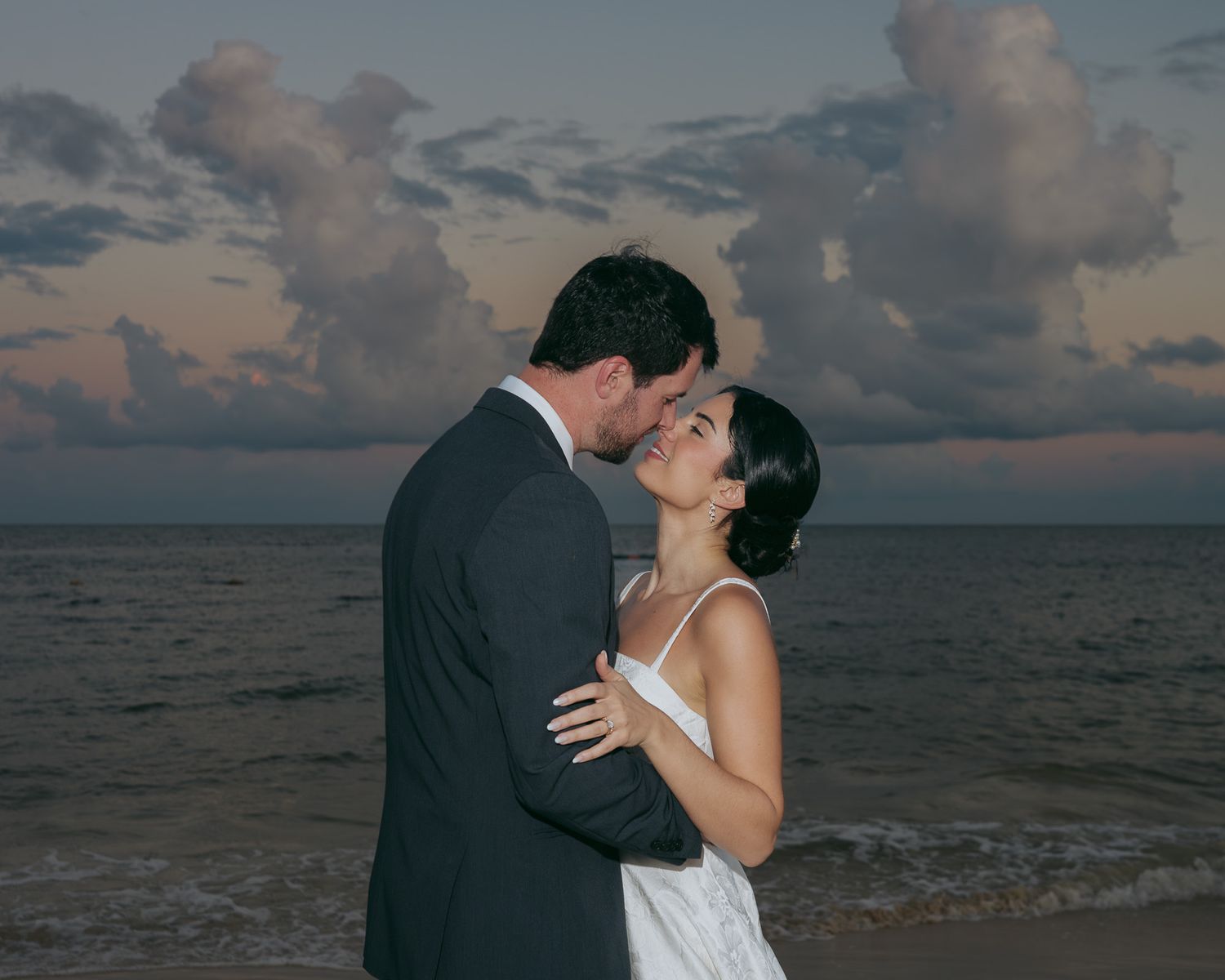 Romantic sunset beach wedding photo of a couple embracing against an ocean backdrop.